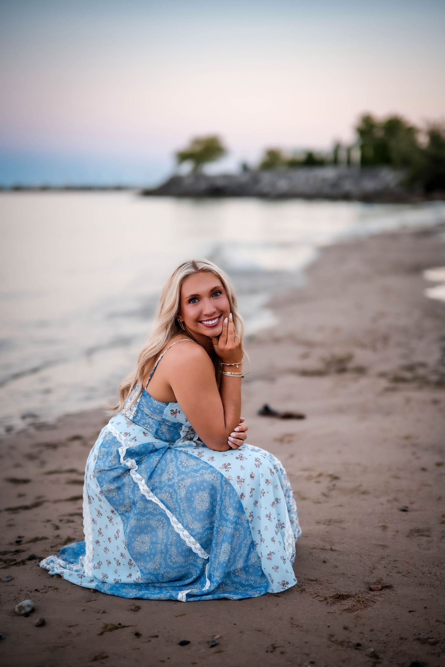 Senior girl sitting in the sand in a blue maxi dress on the Lake Michigan beach