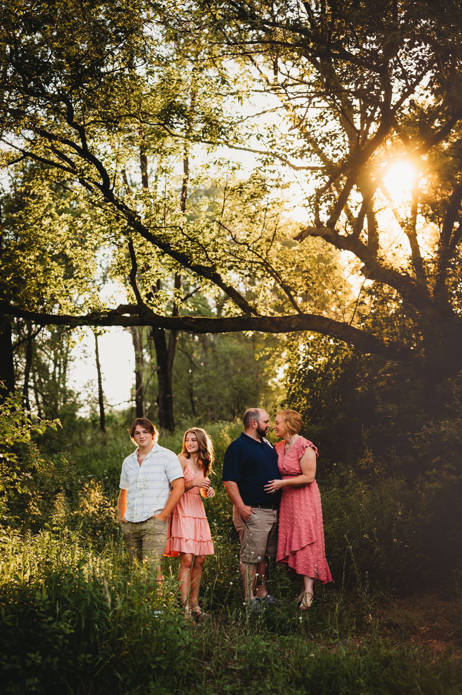 A group stands together in a wooded area at sunset with golden light filtering through tree branches.