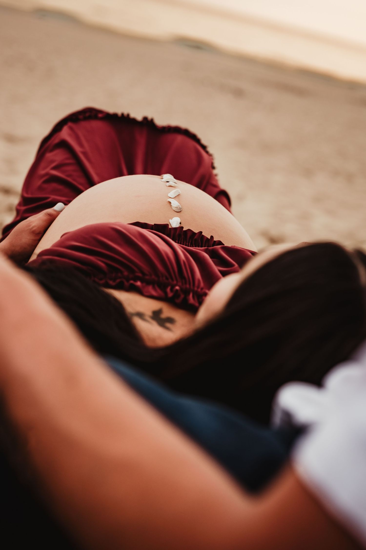 Maternity photo showing pregnant belly with jeweled belly chain in burgundy dress.