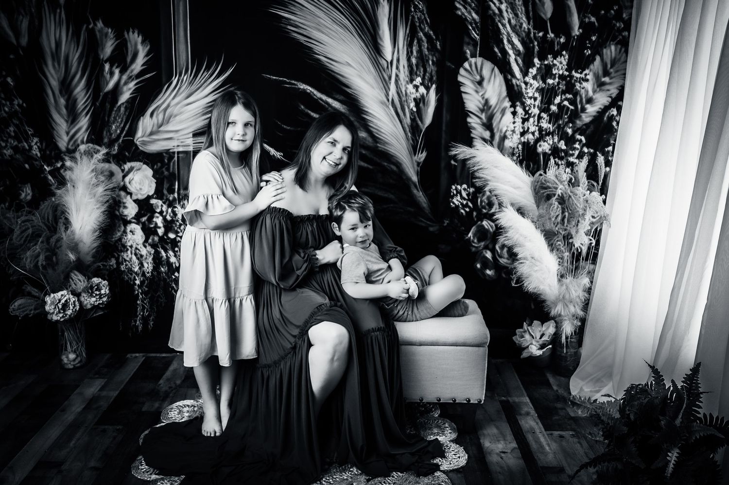 Black and white family portrait with dramatic feather and floral backdrop.