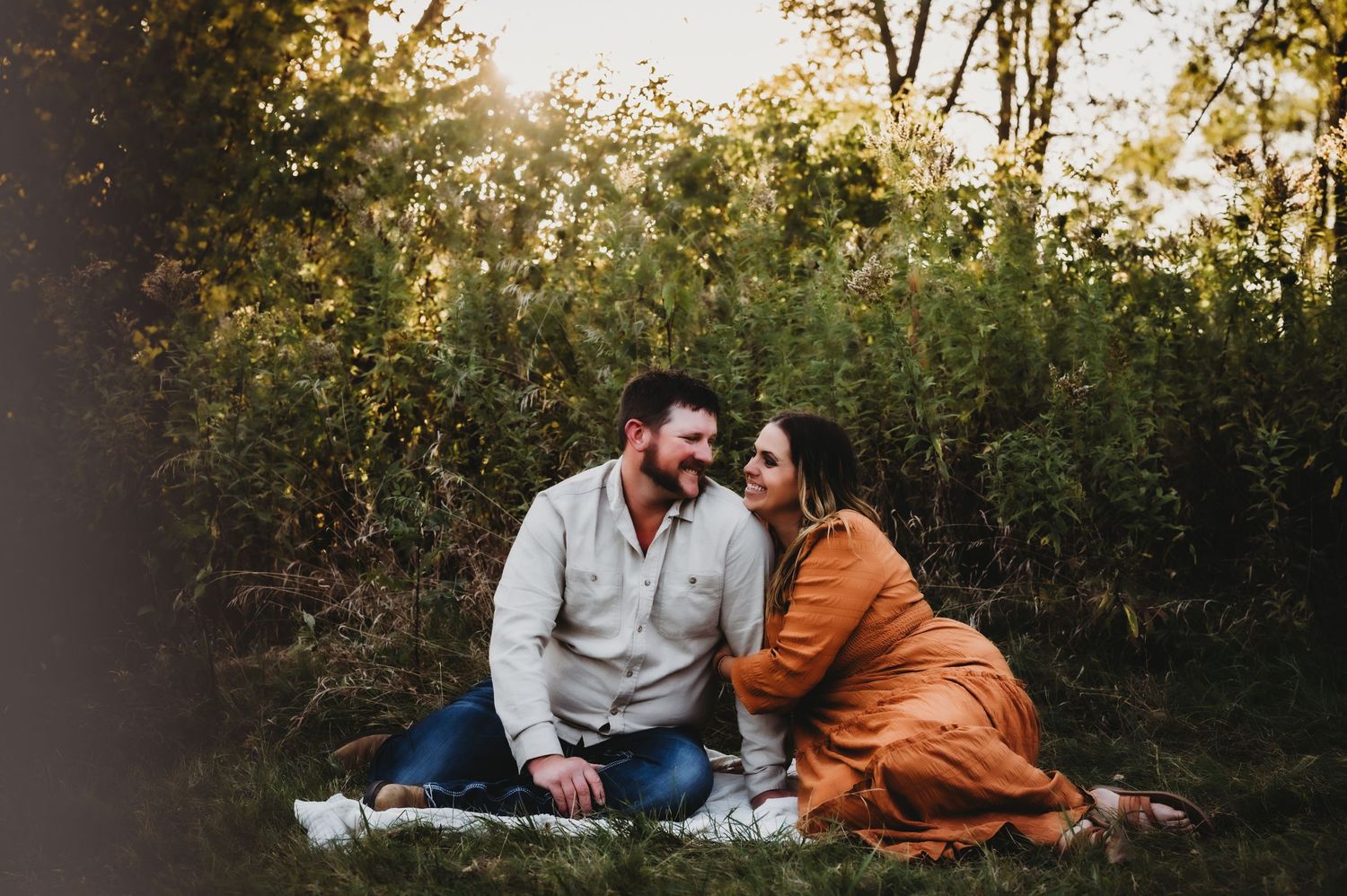 Couple sitting on blanket sharing intimate moment during sunset in outdoor natural setting.
