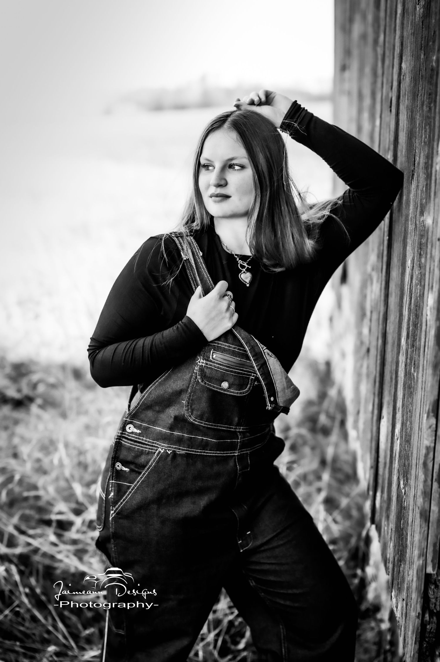 Black and white portrait in overalls against rustic wooden backdrop.
