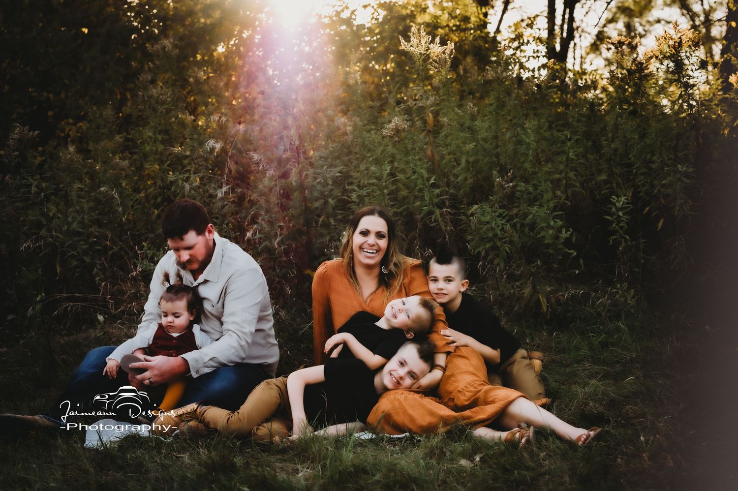 A family relaxes together on the grass during sunset with golden lighting in the background.