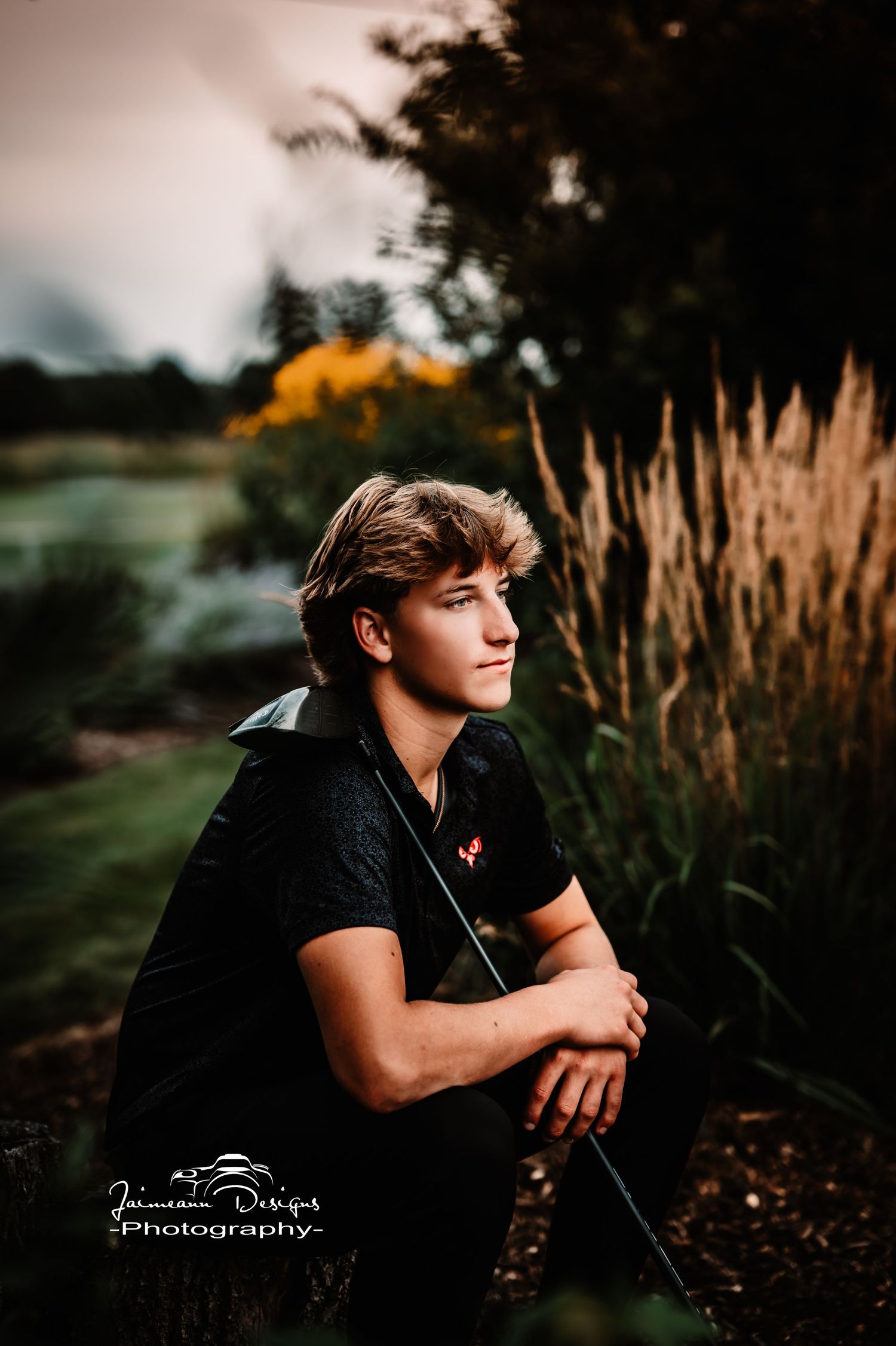 Portrait of golfer with golf club against ornamental grasses at sunset.