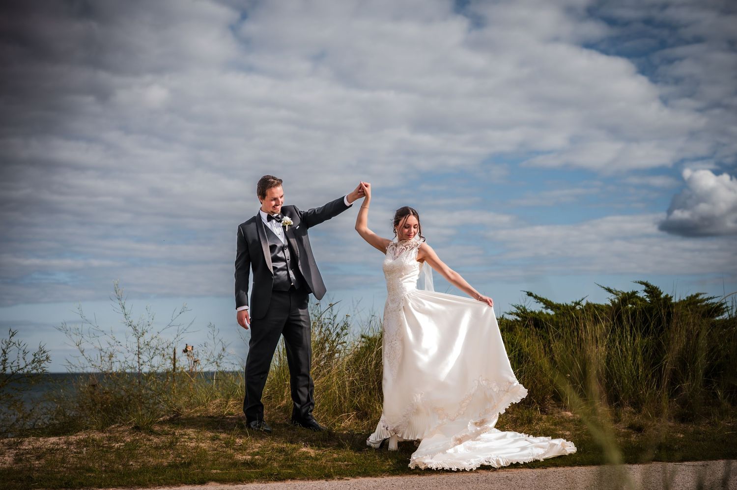 Newlyweds pose together against dramatic cloudy skies in outdoor wedding photos at the beach on the shores of Sheboygan, WI Blue Harbor