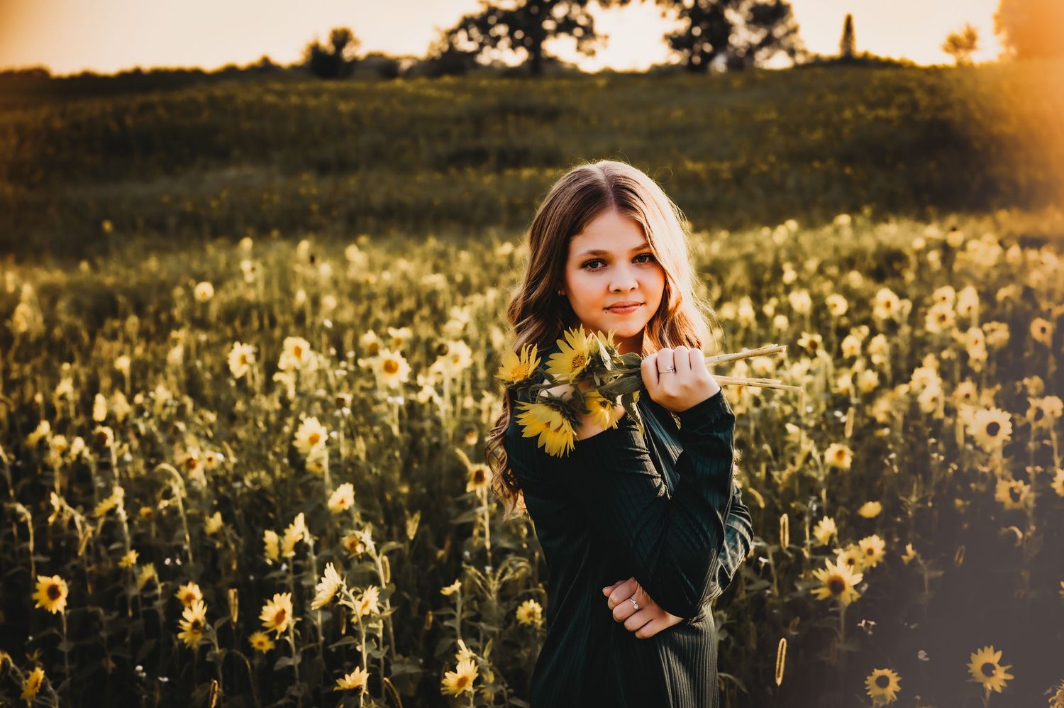 A golden sunset illuminates a field of yellow wildflowers with a figure in a dark sweater standing among the blooms.
