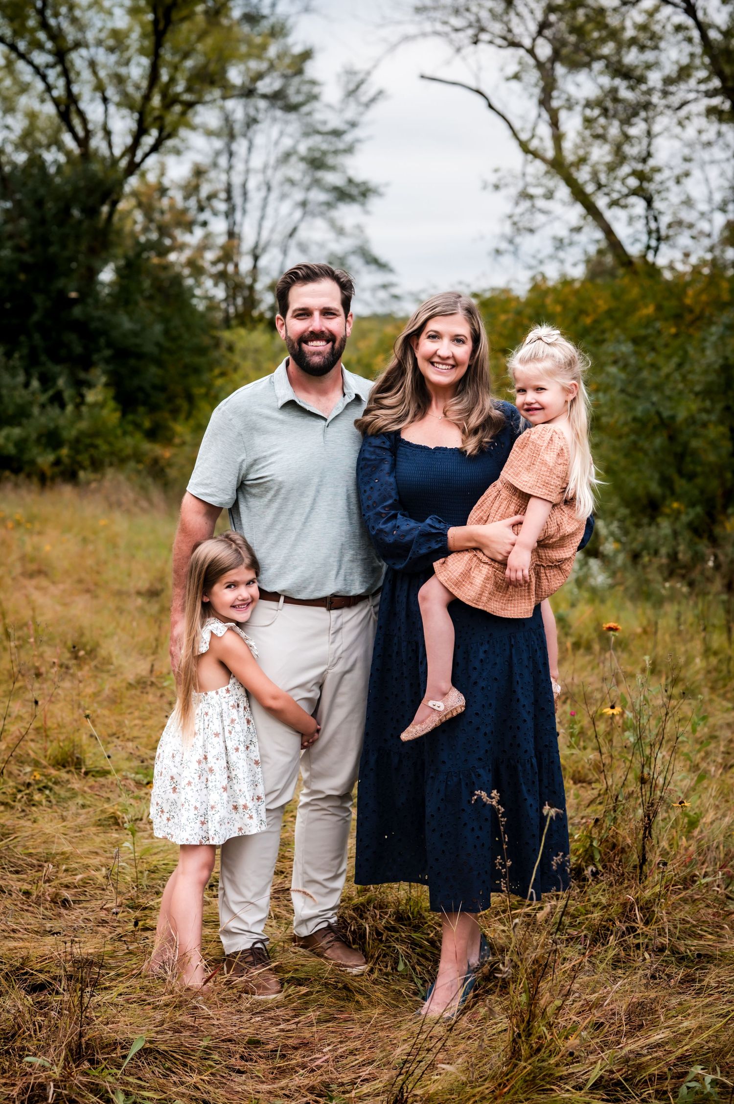 A family poses together in a grassy outdoor field wearing coordinated navy and neutral colored outfits near Hartford, WI