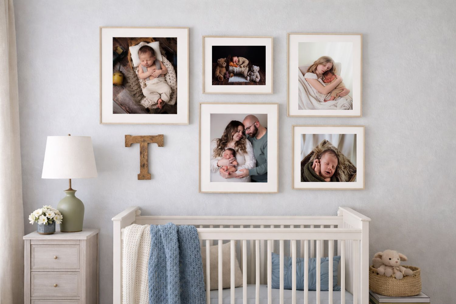 Nursery gallery wall with framed newborn and family photos above a white crib with blue blanket and bedside lamp.