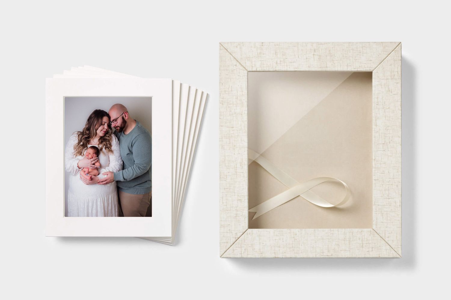 Family photo prints displayed in white matte frames beside an elegant cream linen keepsake box with satin ribbon.
