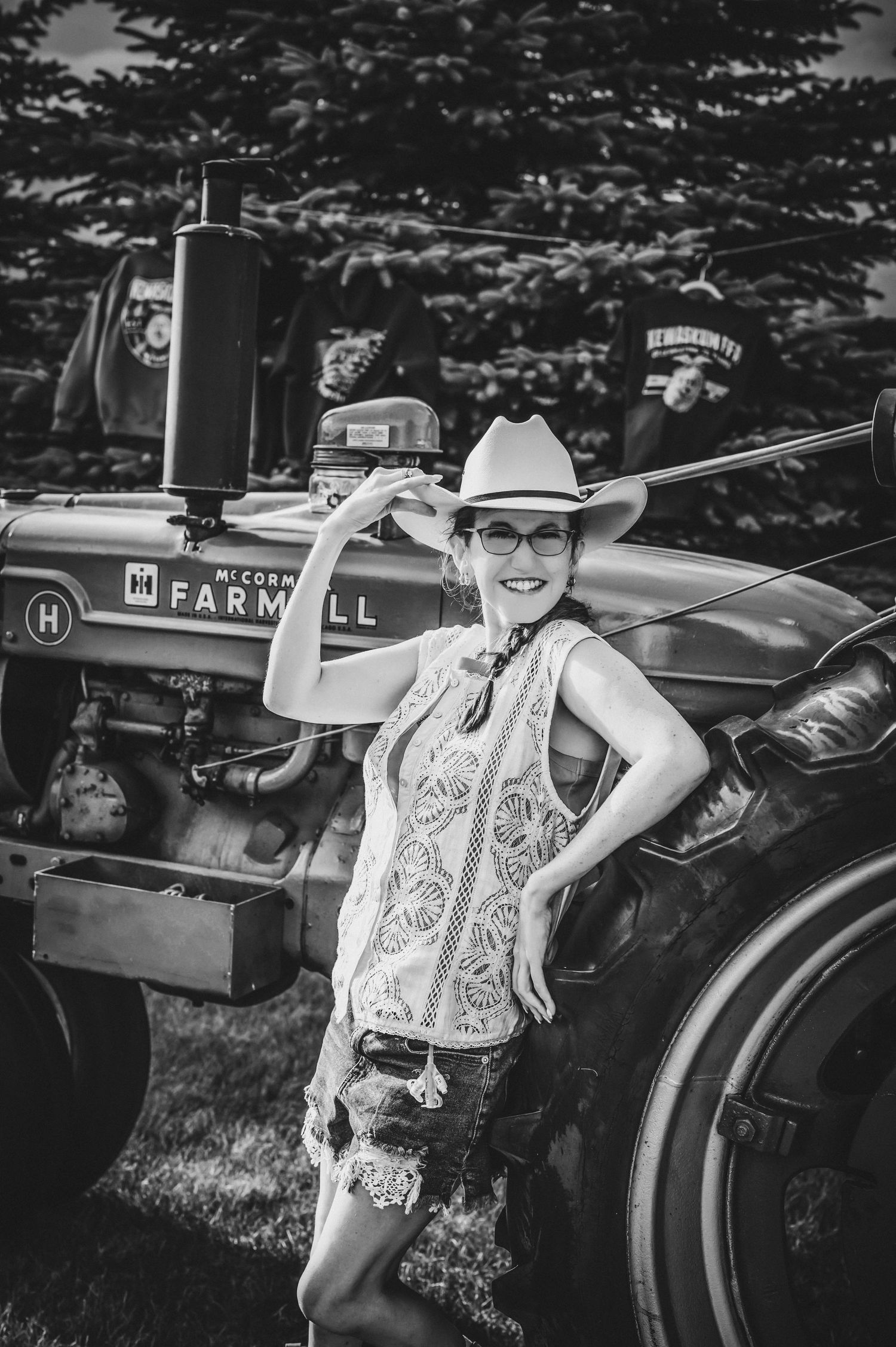 Woman in cowboy hat posing beside vintage McCormick Farmall tractor, black and white photo.