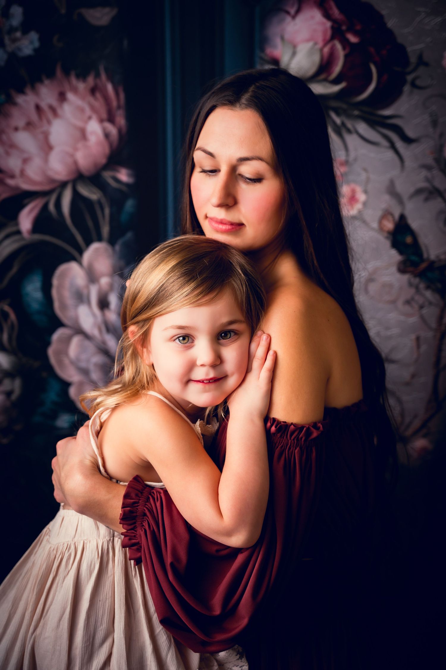 Intimate portrait against dark floral wallpaper featuring burgundy and cream dresses.