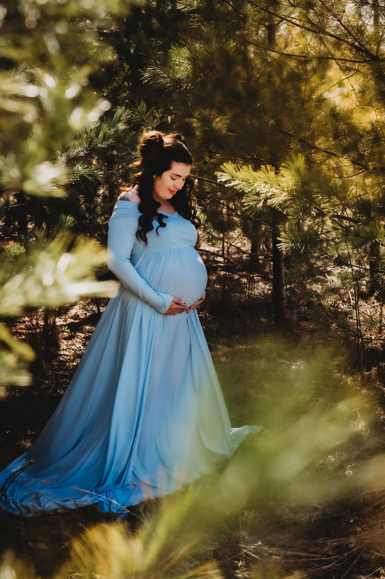 Dreamy outdoor maternity photo with soft sunlight filtering through forest trees.