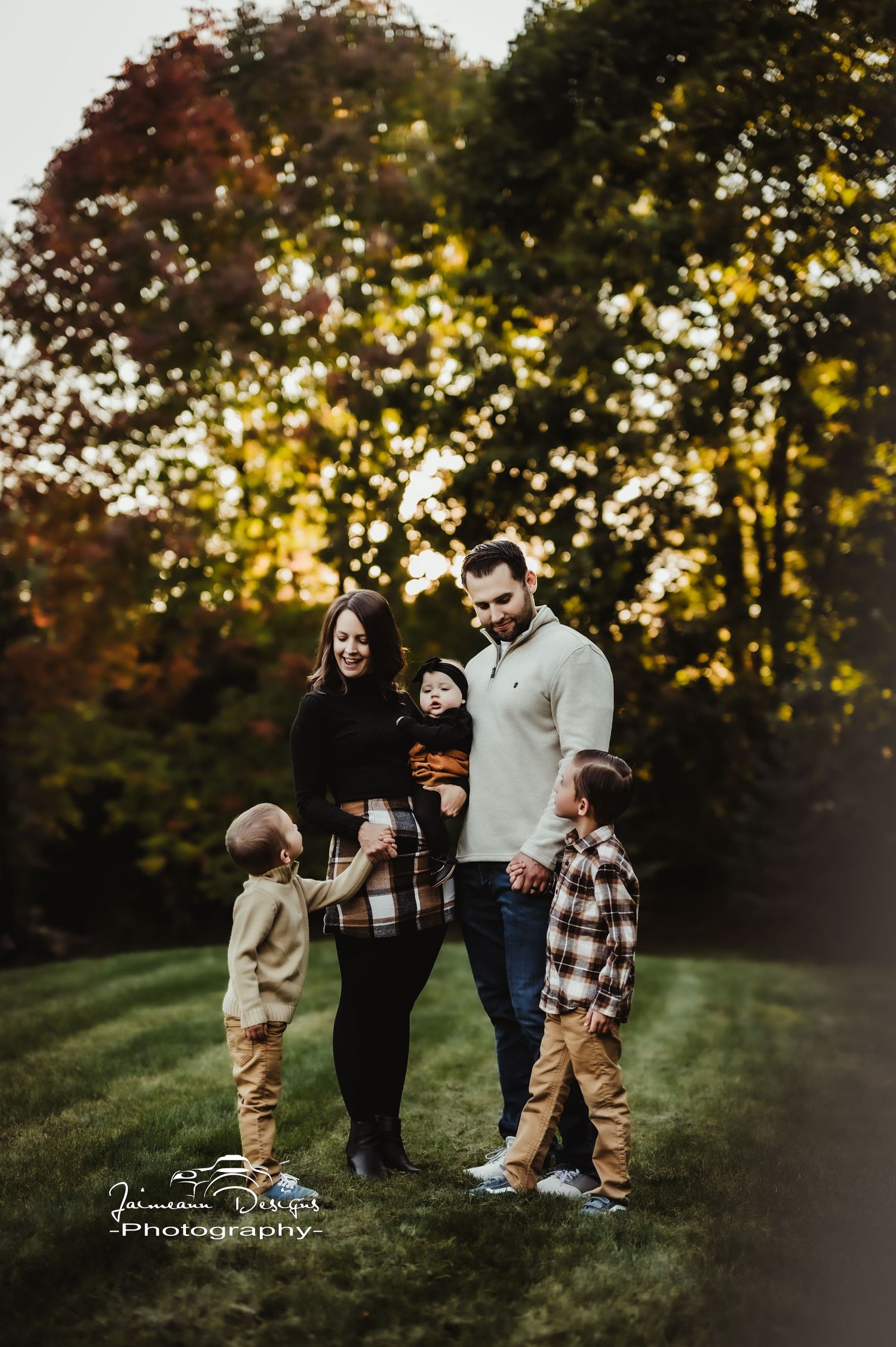 A family stands together outdoors with golden autumn trees in the background.