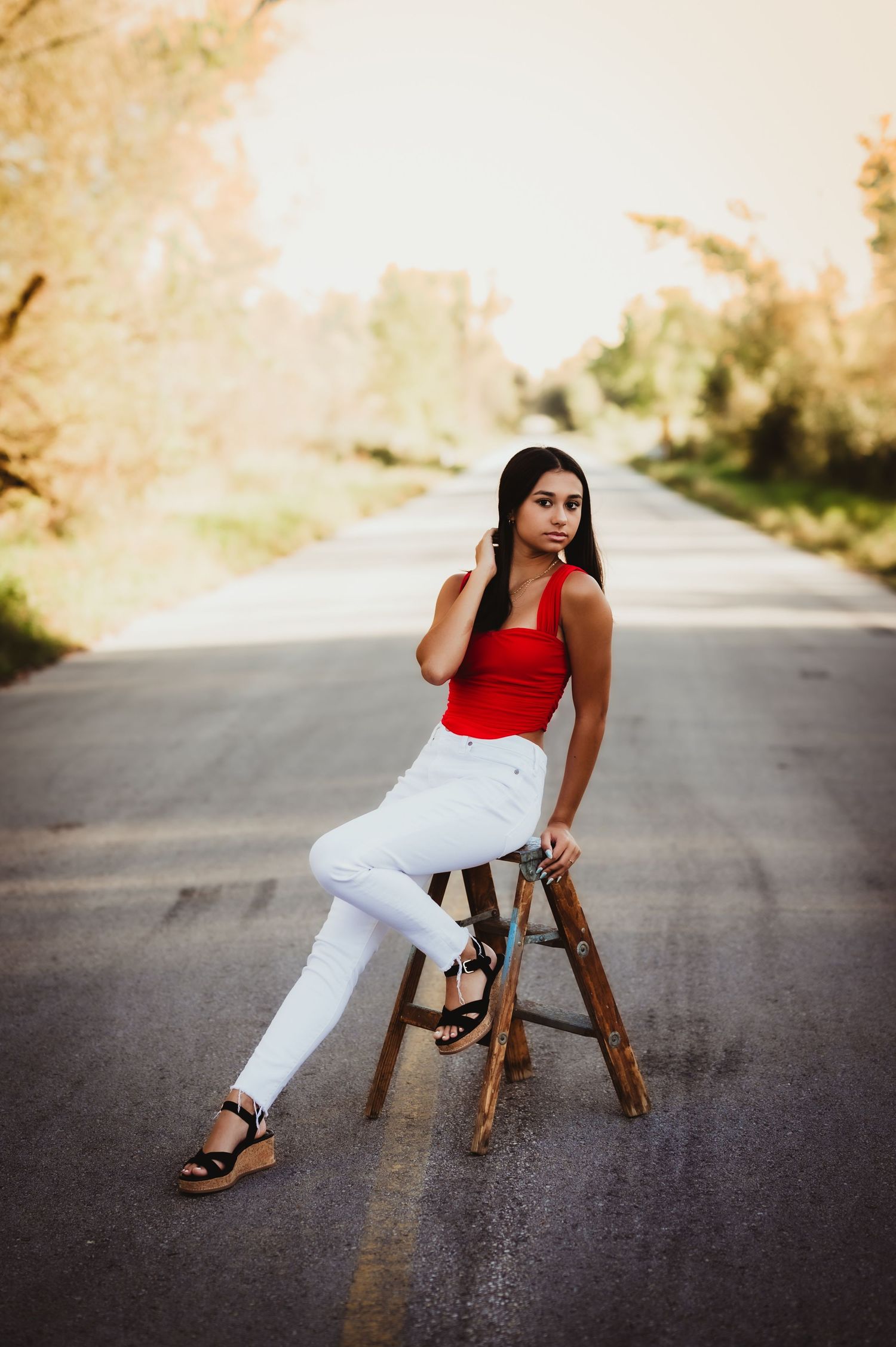 A fashion portrait featuring a red top and white pants with a wooden ladder on a rural road.