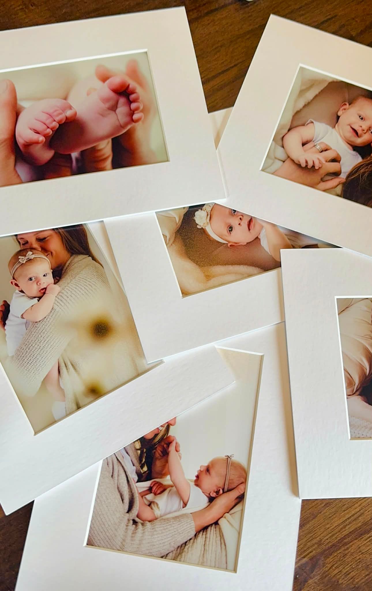 Collection of matted newborn baby photos on wood table, featuring infant feet, mother and baby portraits.