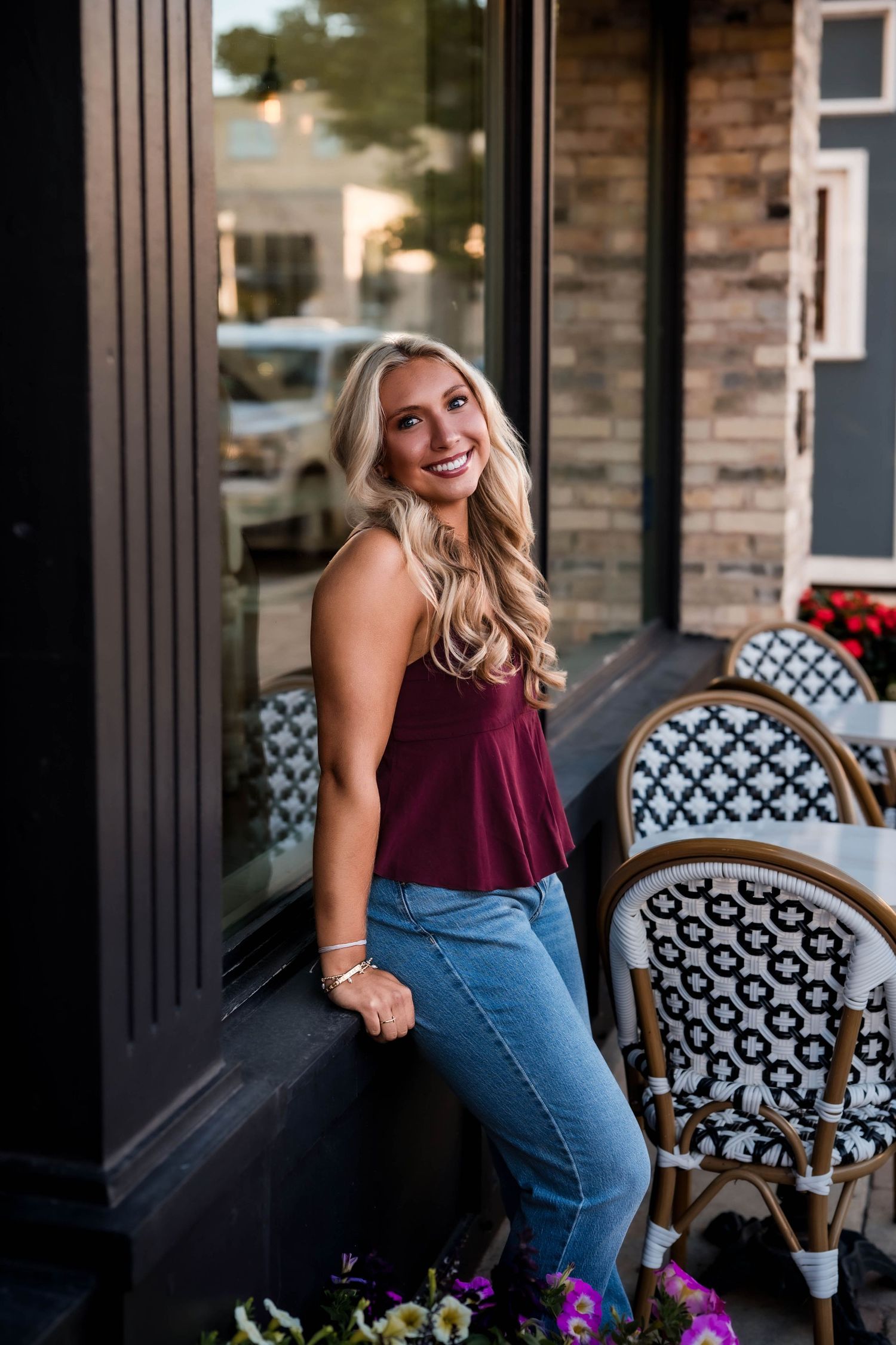 Senior girl in a burgundy top leaning on a storefront window in downtown Port Washington