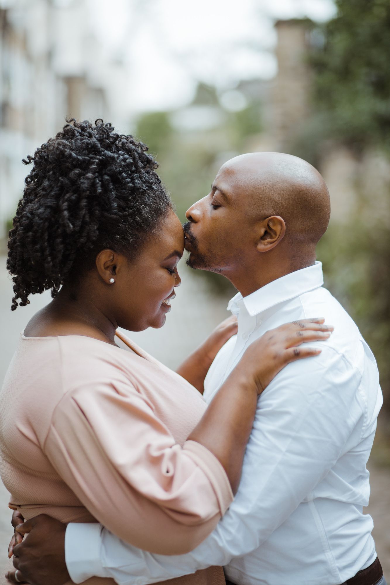 A loving Black couple shares a tender moment, embracing and about to kiss outdoors in a romantic urban setting.
