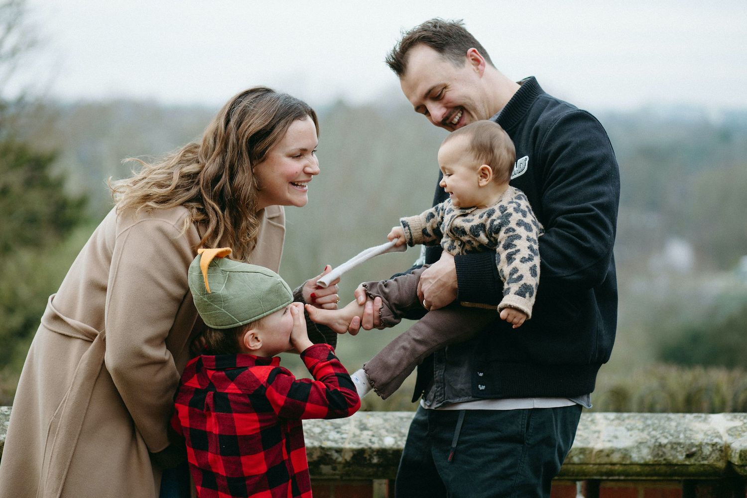 Happy family with two children sharing a laughter outdoors, smiling together in a scenic garden setting.