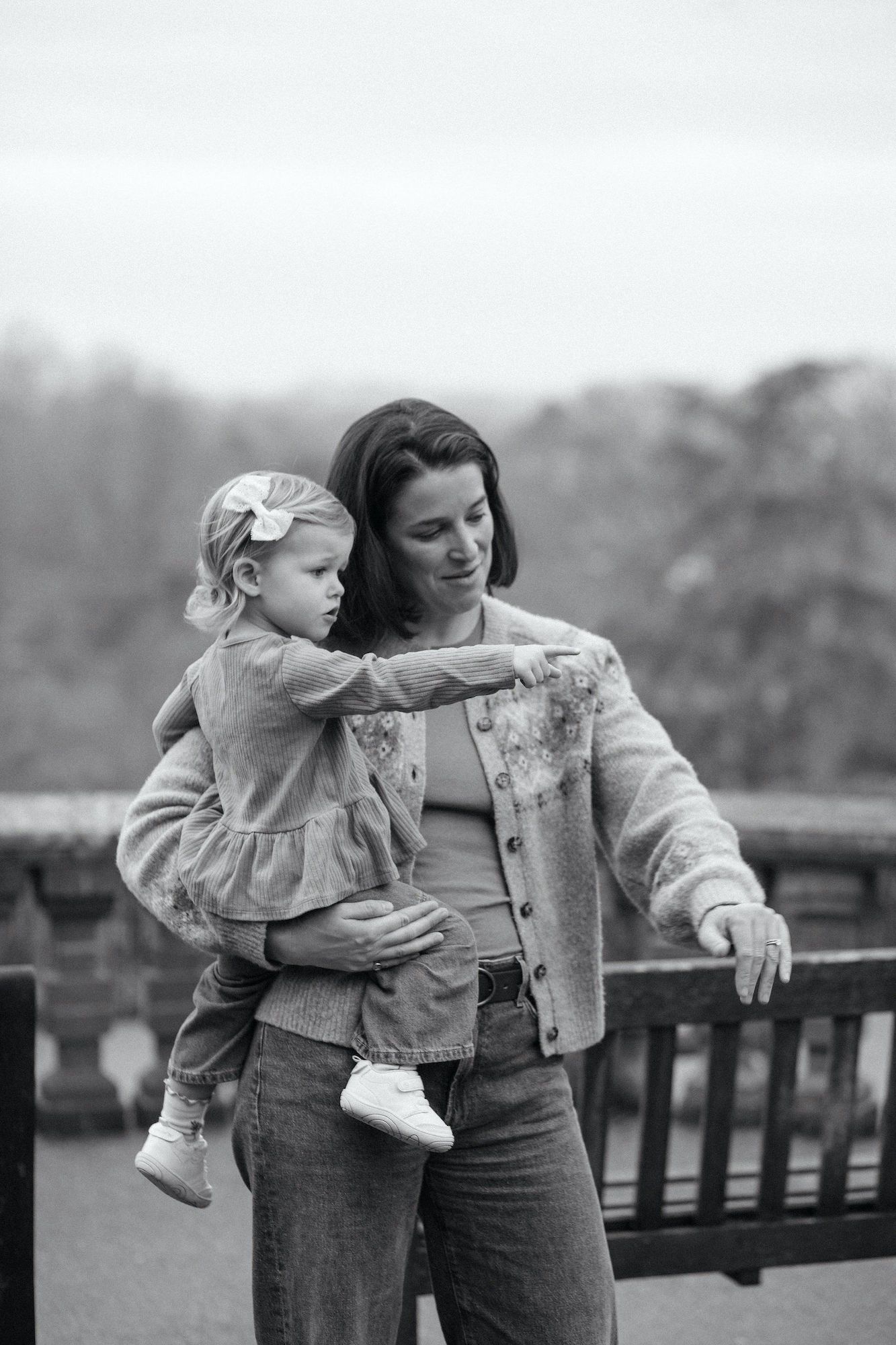 Black and white photo of a mother holding her young daughter outdoors, as the child points at something in the distance.