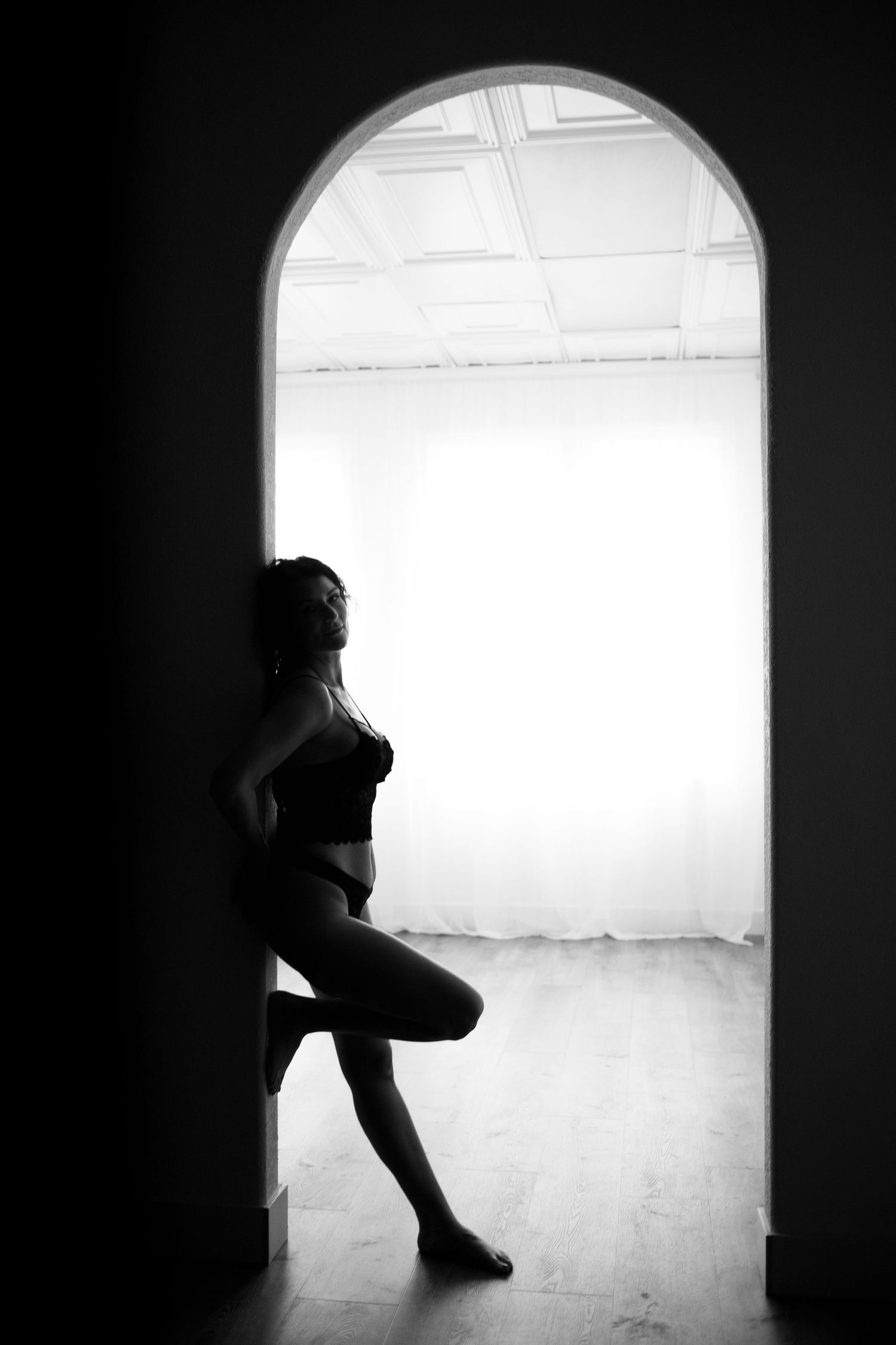 A boudoir photo of black and white photo of a woman in lingerie in a doorway.