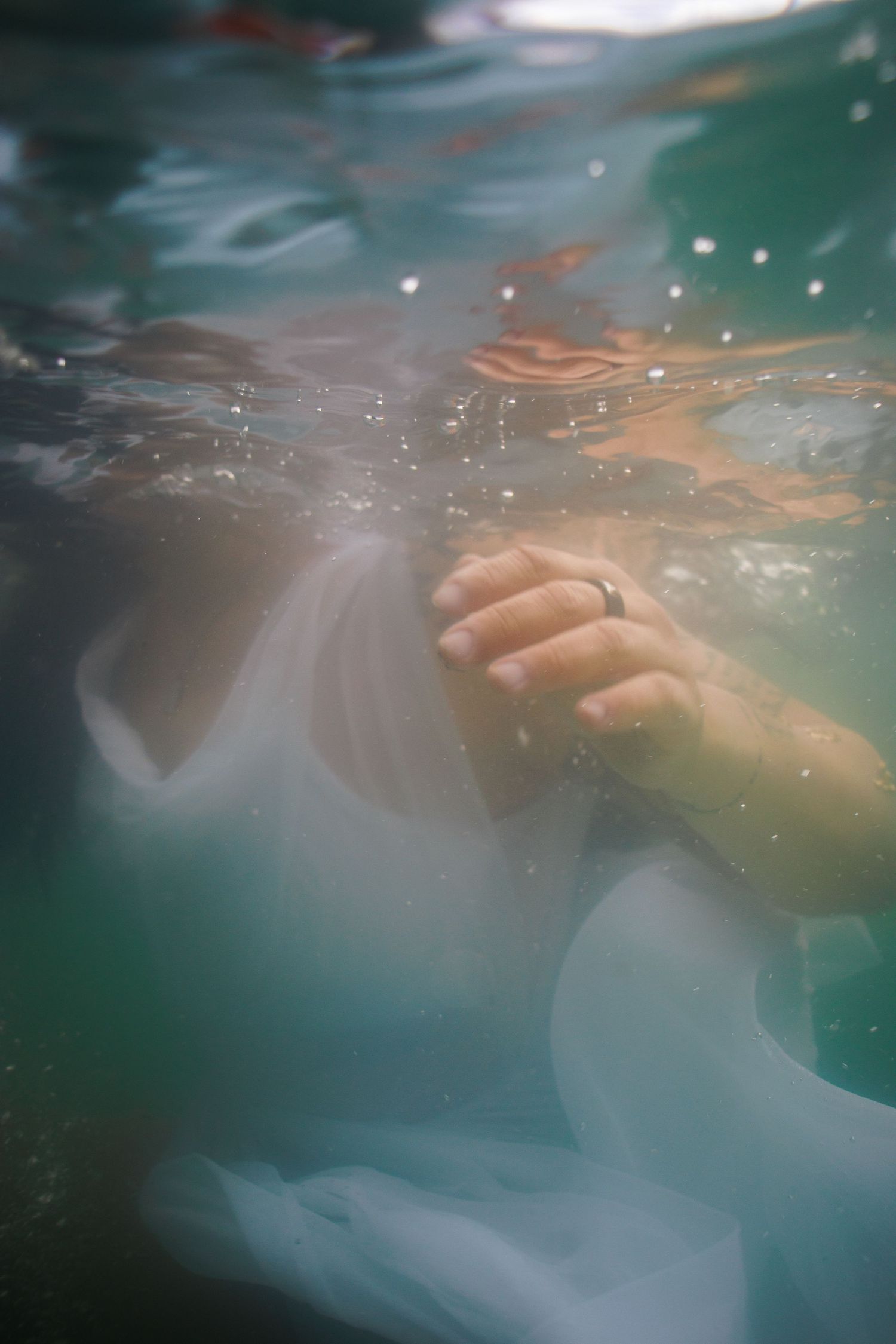 An underwater photo of a woman in a white dress swimming in green water.