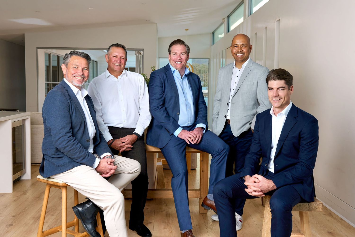 Senior leadership team in suits smiling together in a modern bright office space for a corporate team photo. Shot by Studio TingTing.