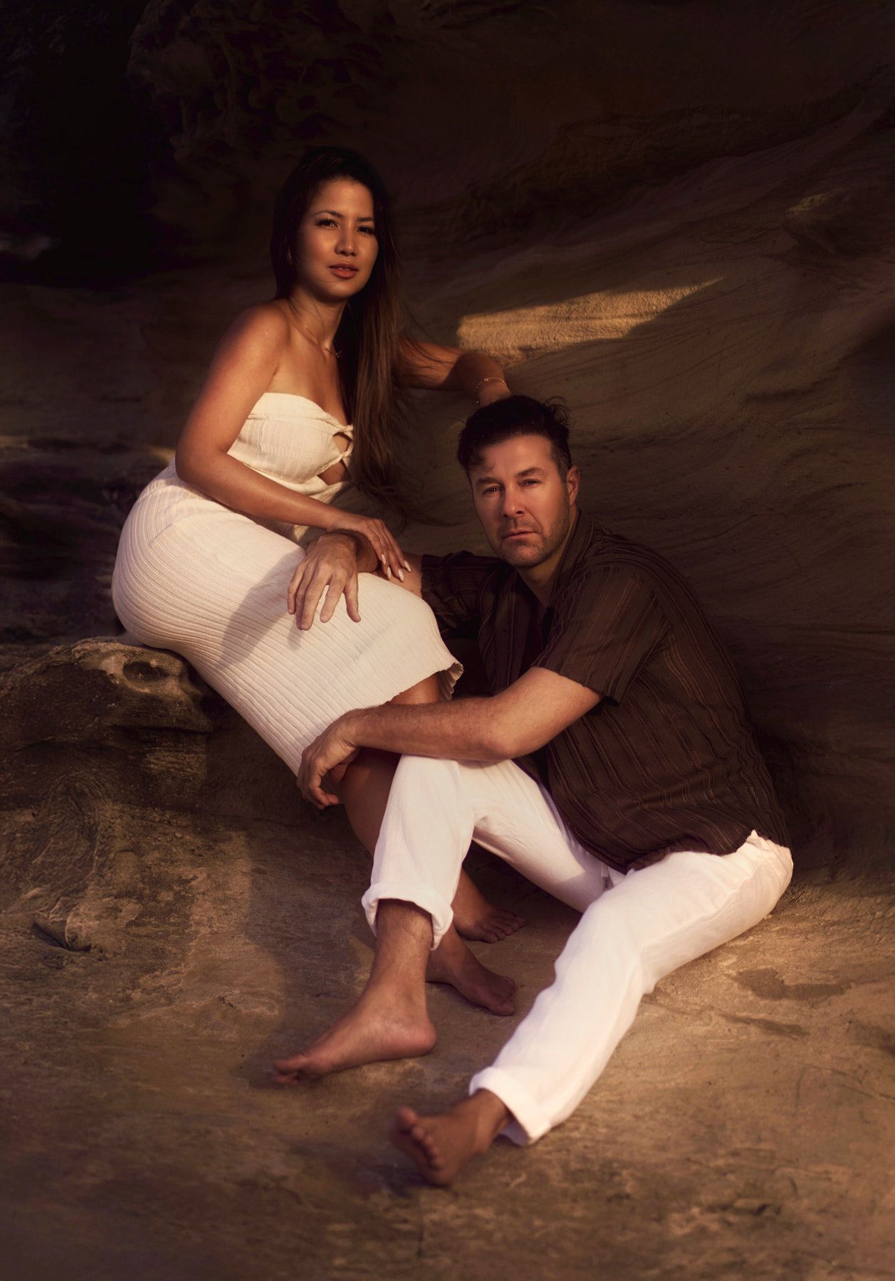 Romantic couple in white outfits pose intimately on rocks during sunset photoshoot in Balmoral beach Sydney by Studio TingTing.