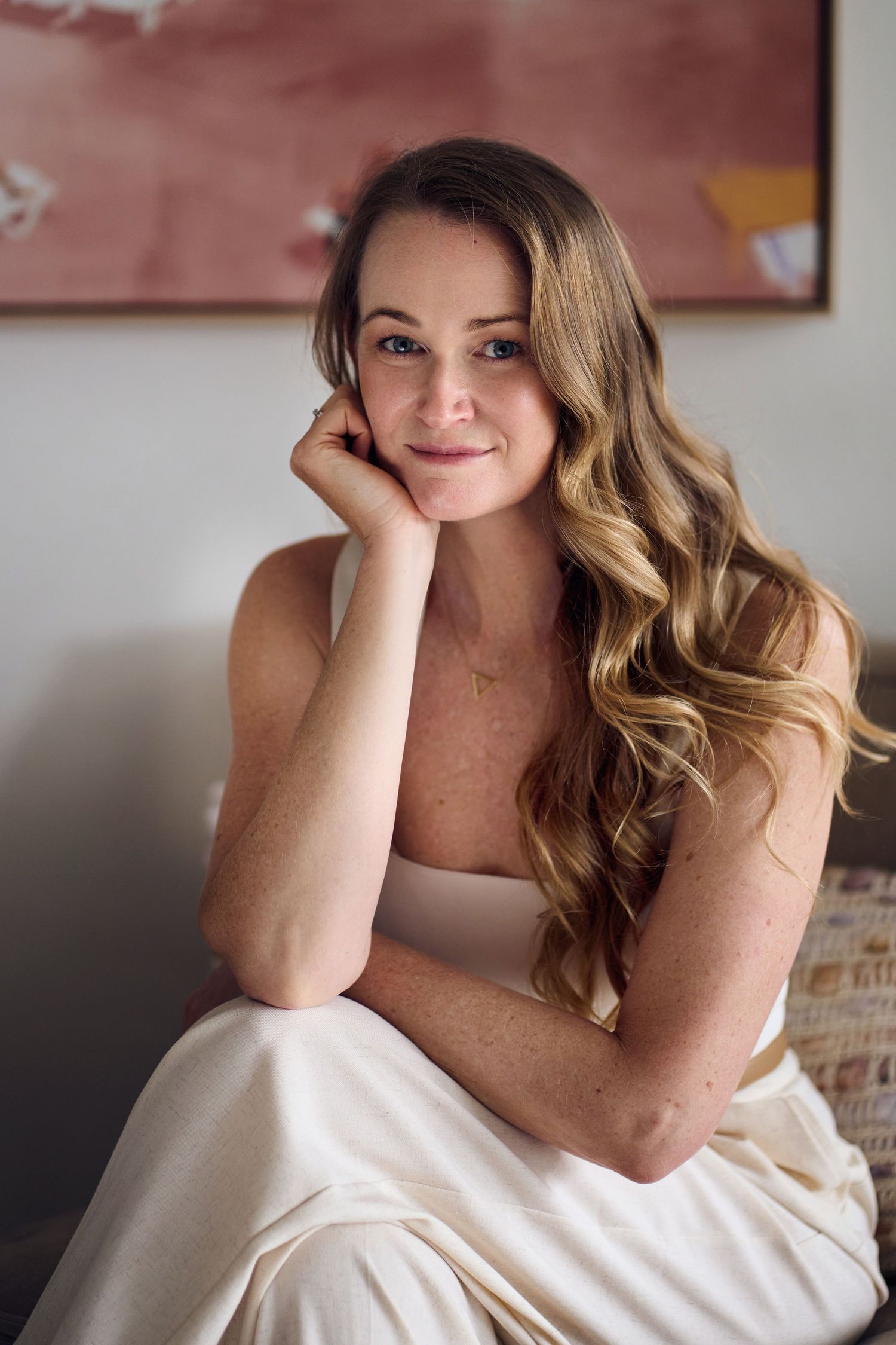Woman in white tank top poses casually on couch with soft lighting and pink wall art by Studio TingTing in sydney.