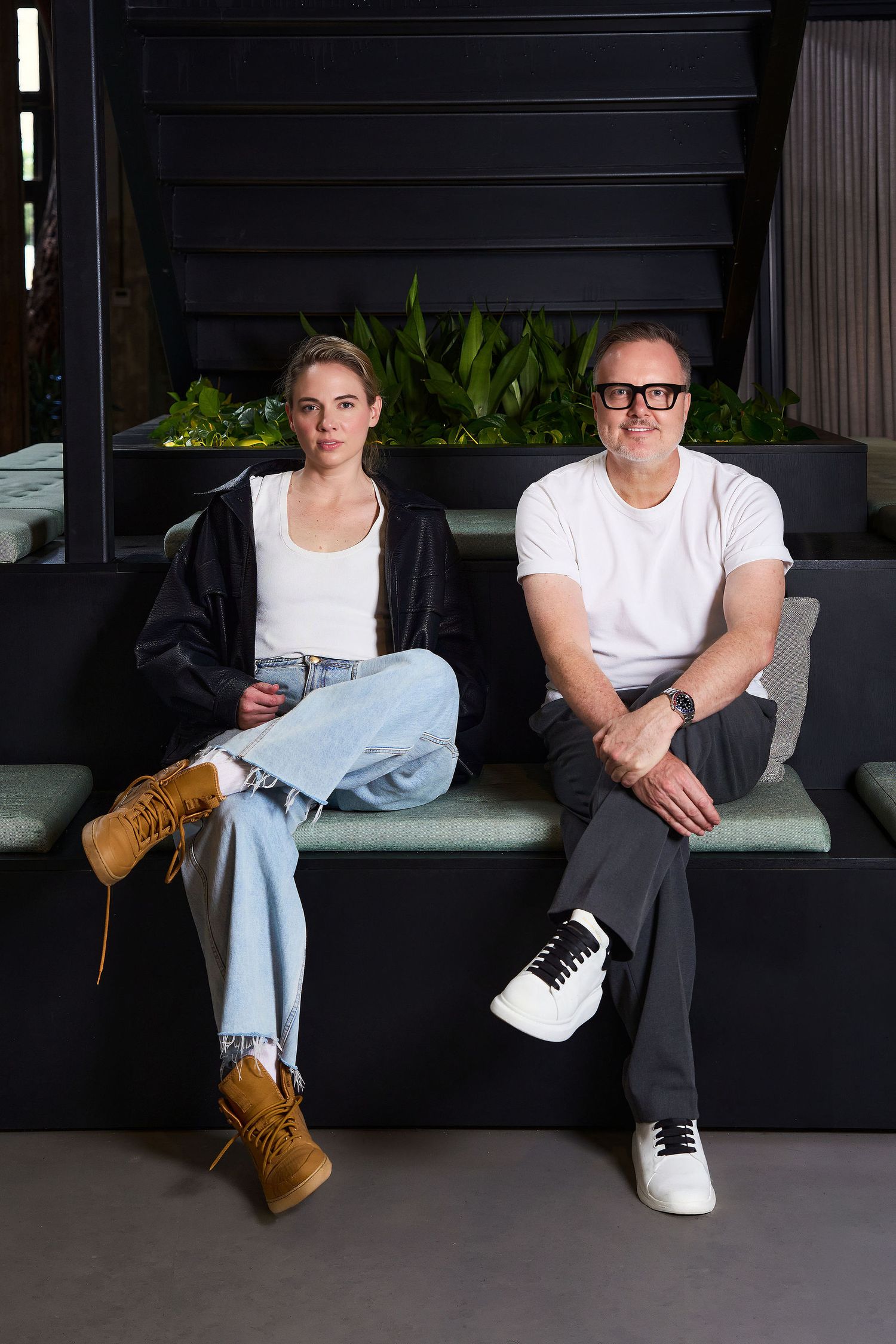 A young woman and middle-aged man sit together on a bench, dressed casually in jeans and white tops.
