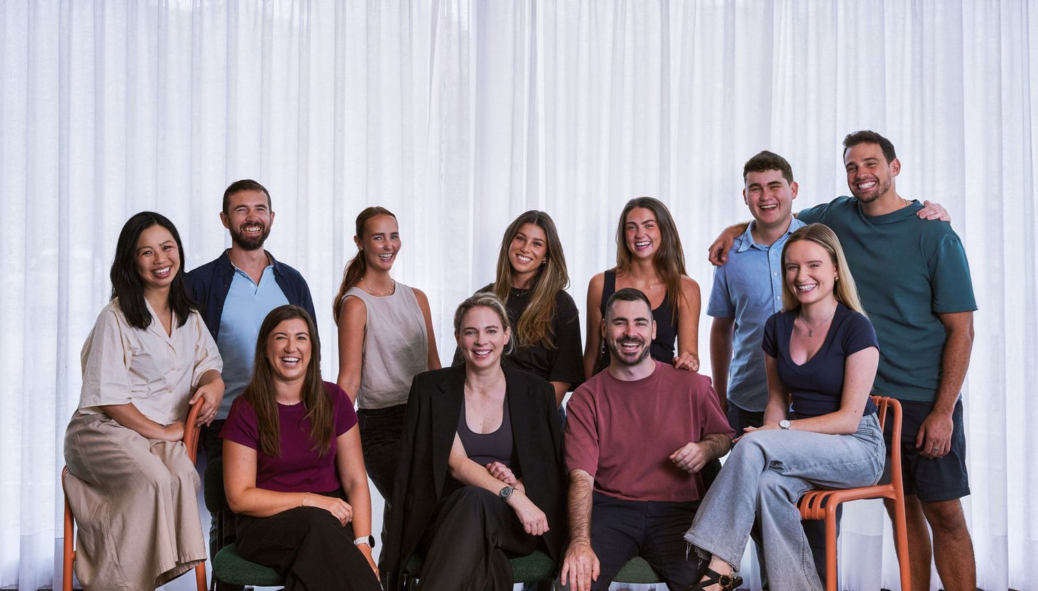 A large group of people in casual attire stand together smiling and posing for a team photo in Sydney office by Studio TingTing.