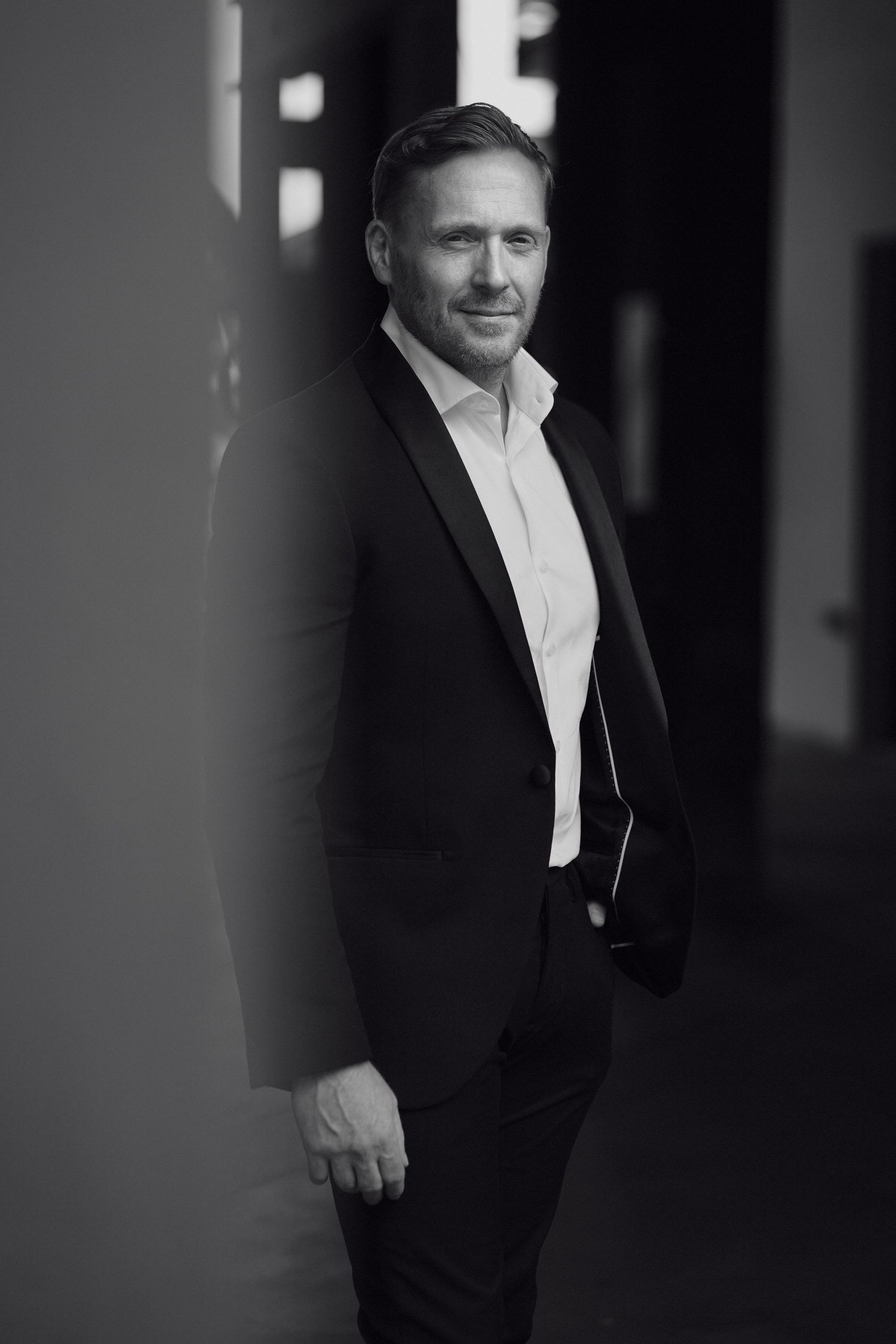 Black and white professional portrait of person in dark suit and white shirt in moody lighting. Studio TingTing.
