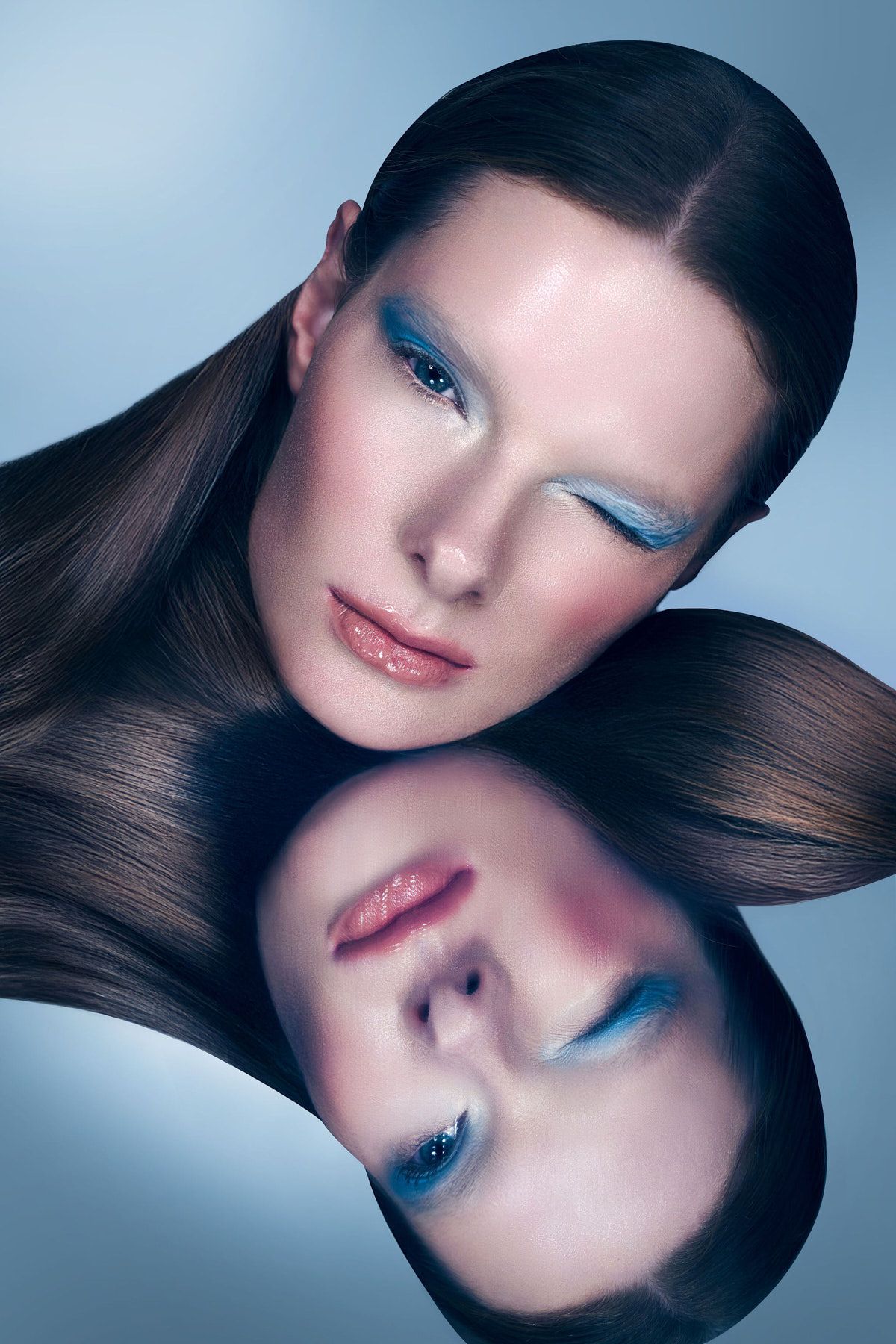 Artistic beauty portrait with mirror effect showing blue eyeshadow and glossy makeup.