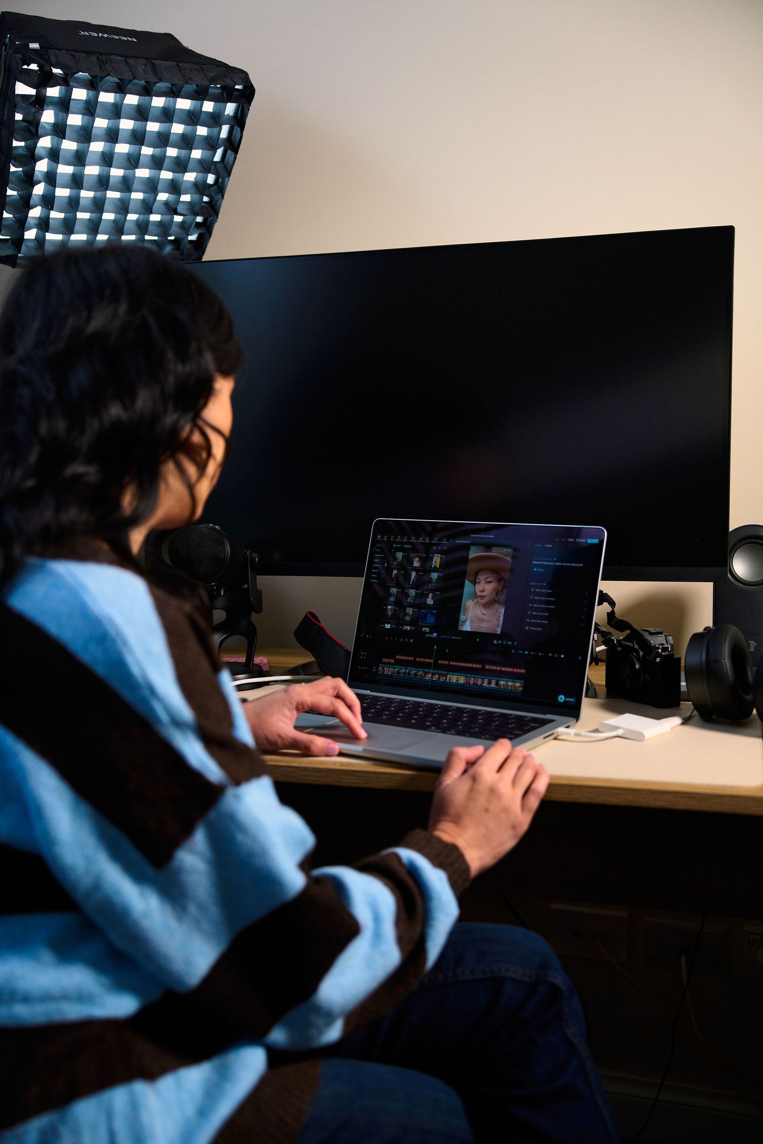 Content creator editing video footage on a laptop at a professional home studio desk with lighting equipment.