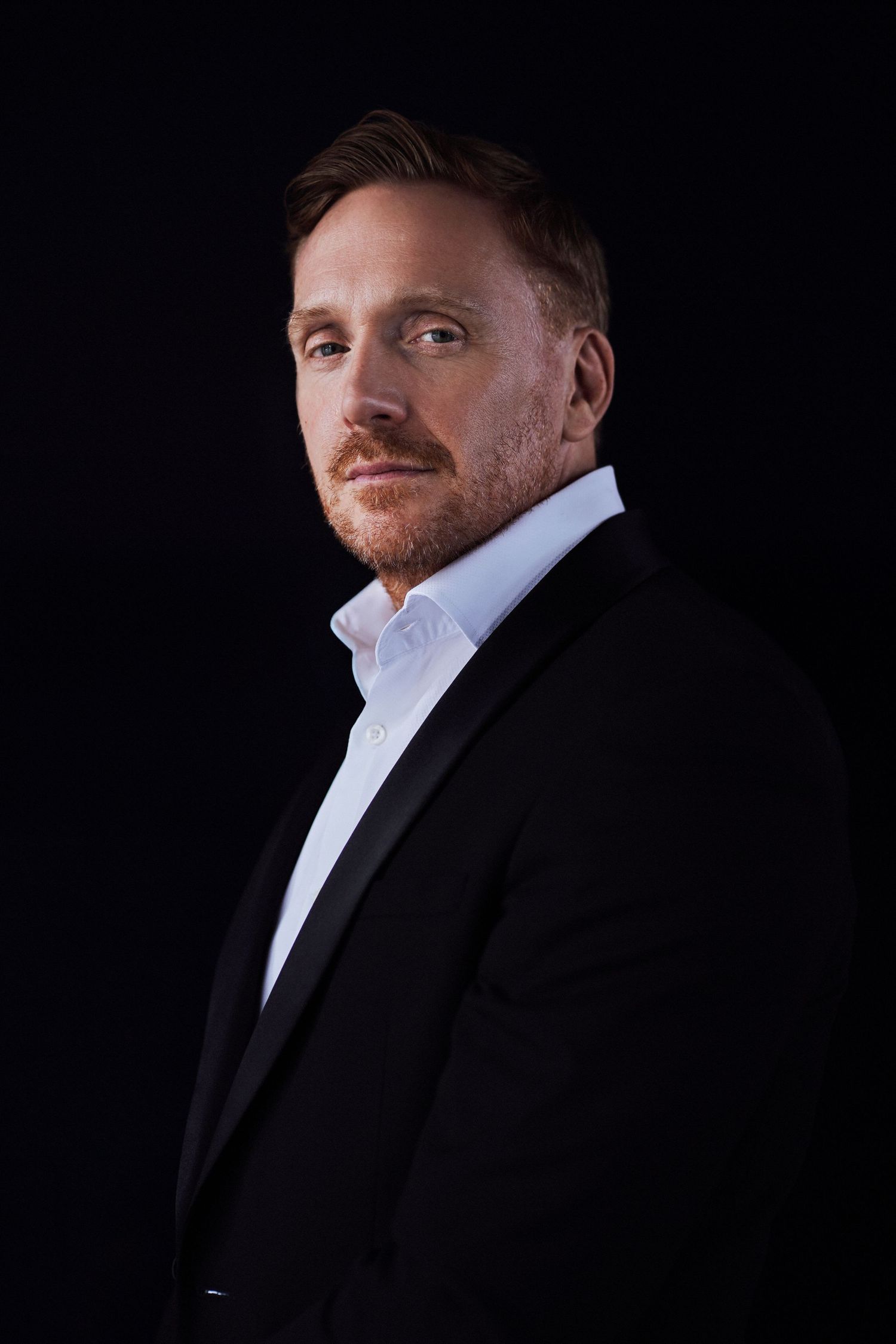 Professional portrait of a man with facial hair wearing a dark suit and white dress shirt against a black background by Studio TingTing.