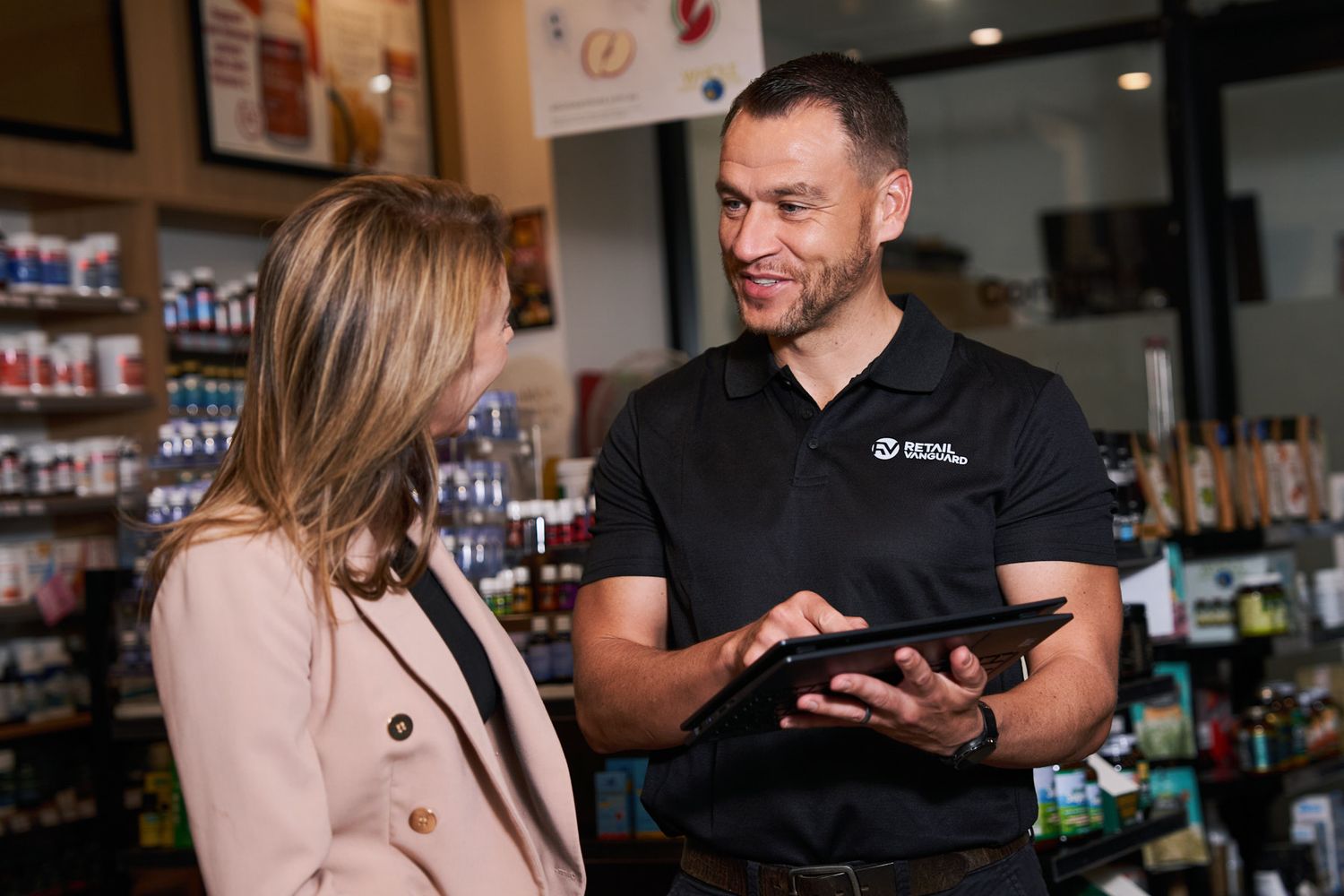 Retail staff member assists customer with digital tablet in store while browsing merchandise shelves. Photo for business website in Sydney.