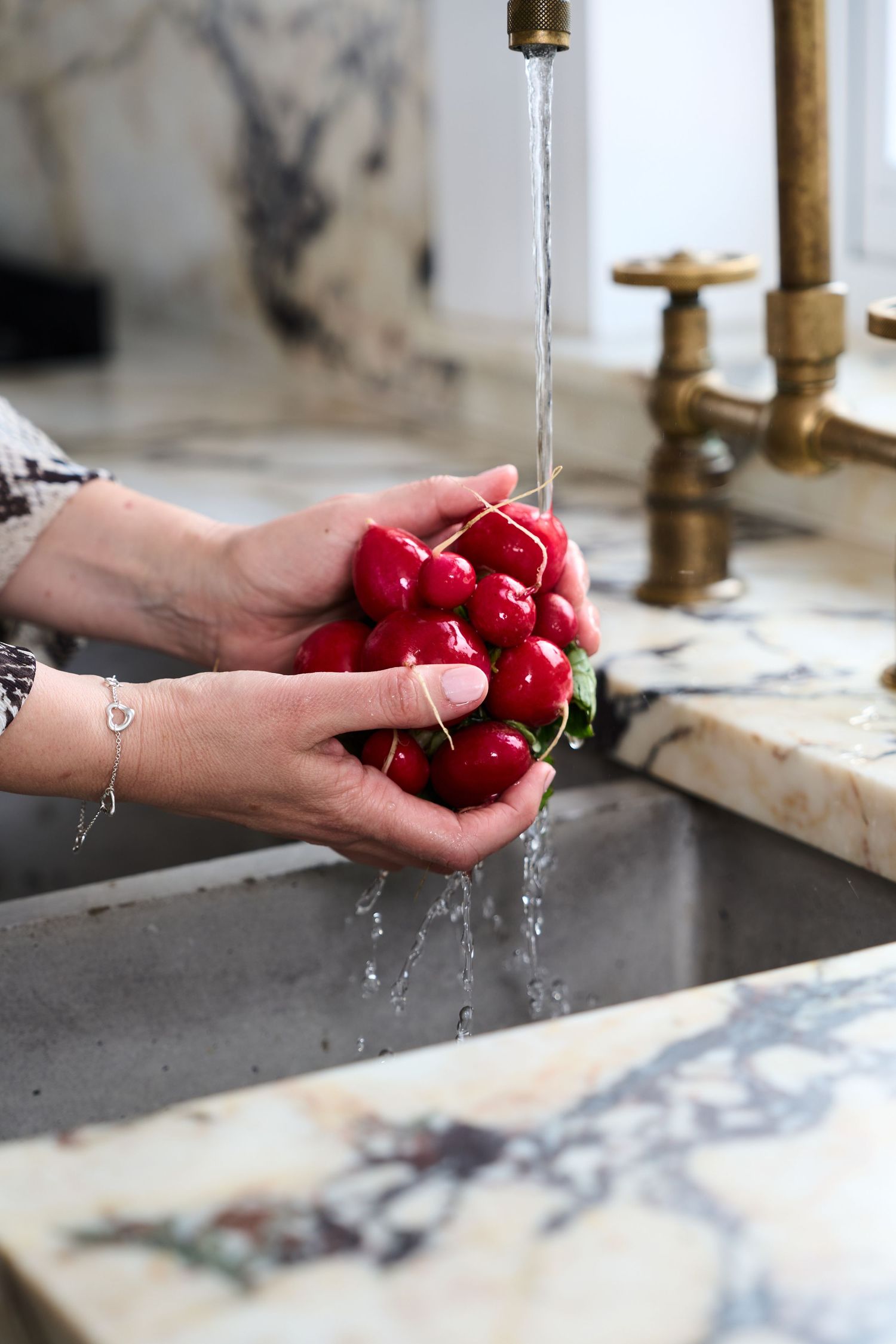 Closed up hands washing fresh red radishes under running water in kitchen sink.
