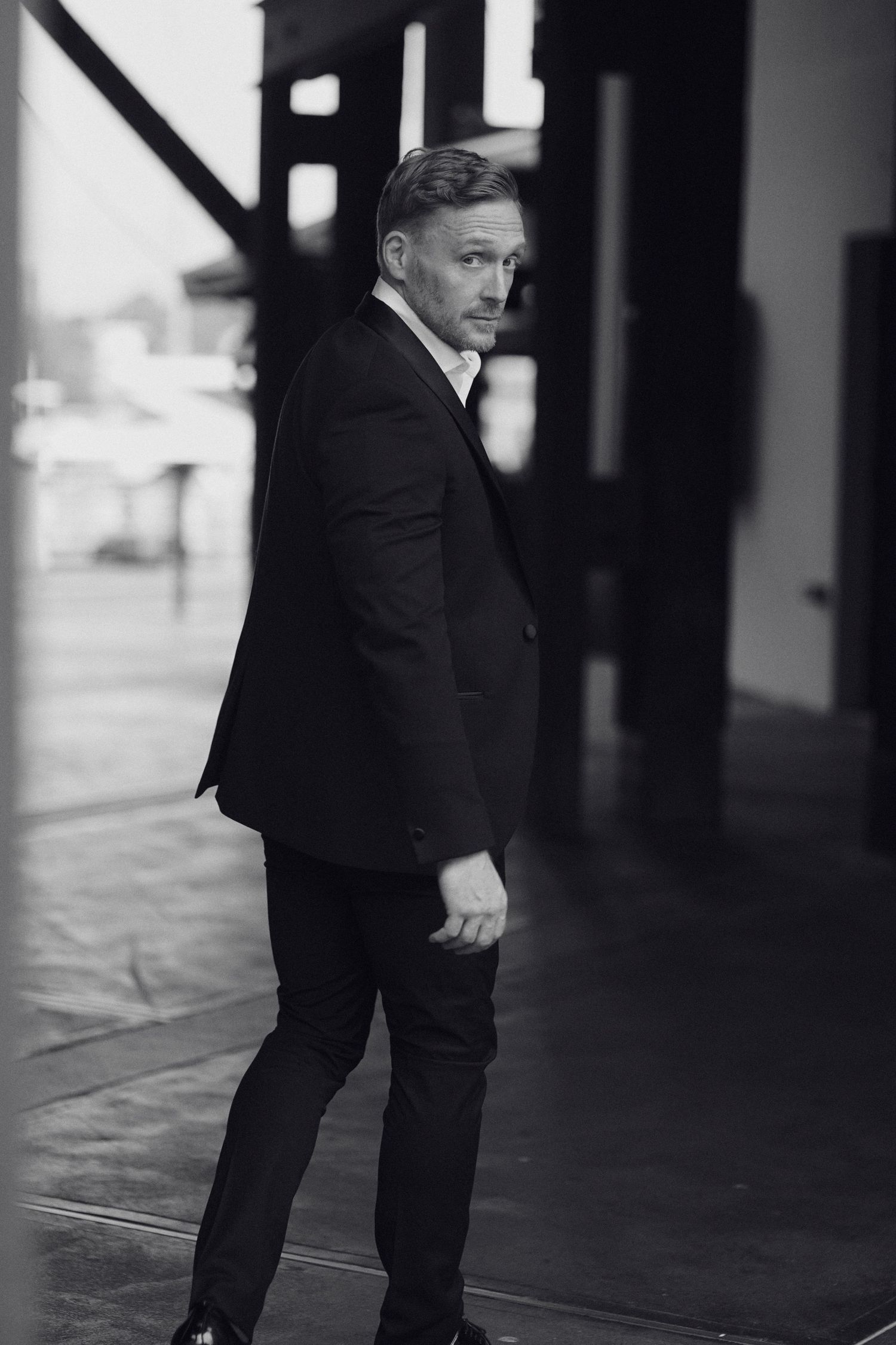 Black and white lifestyle portrait showing sideways stance in dark suit with urban background. Studio TingTing in sydney.