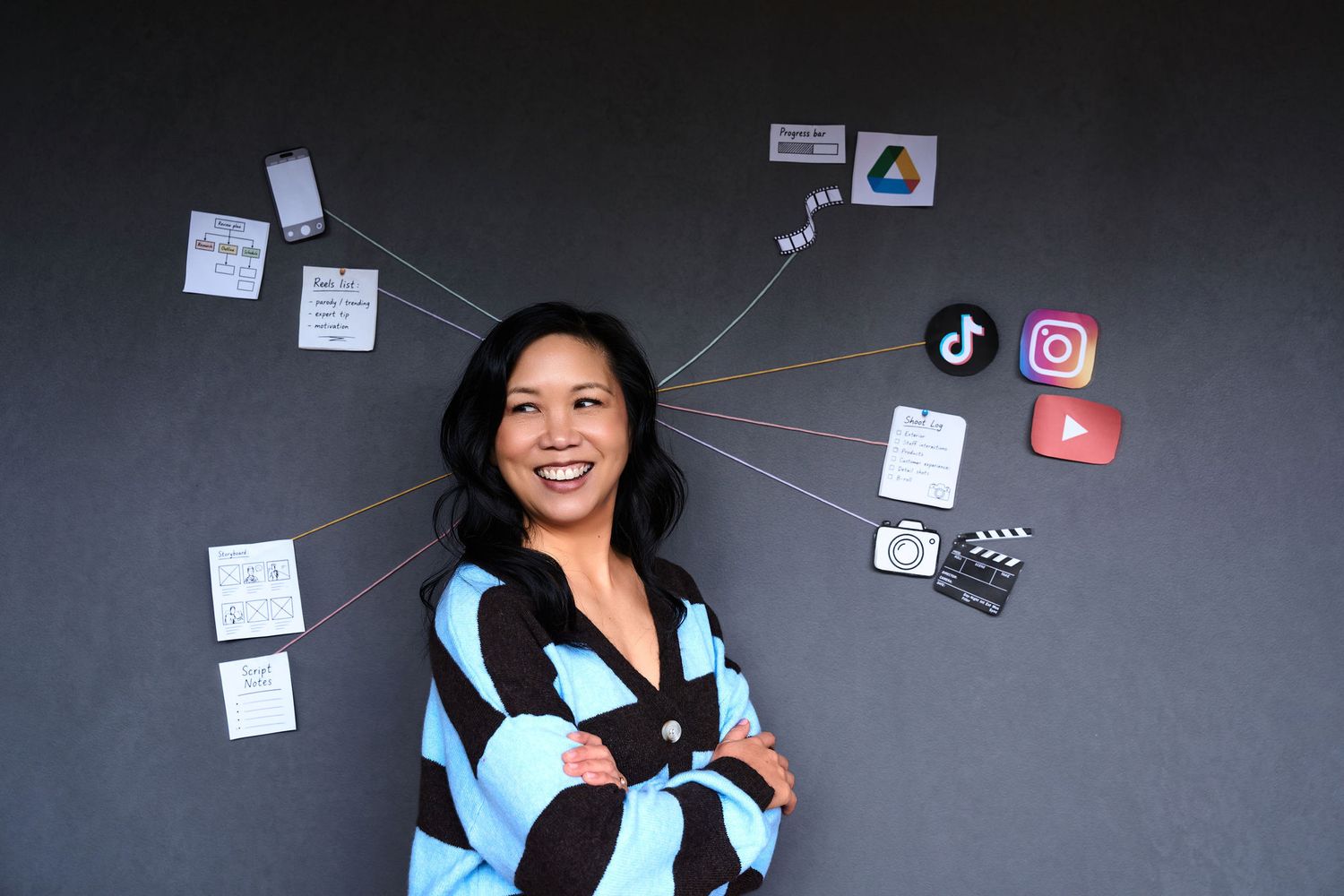 Woman smiling with arms crossed in front of a wall displaying social media icons including TikTok, Instagram, and YouTube.