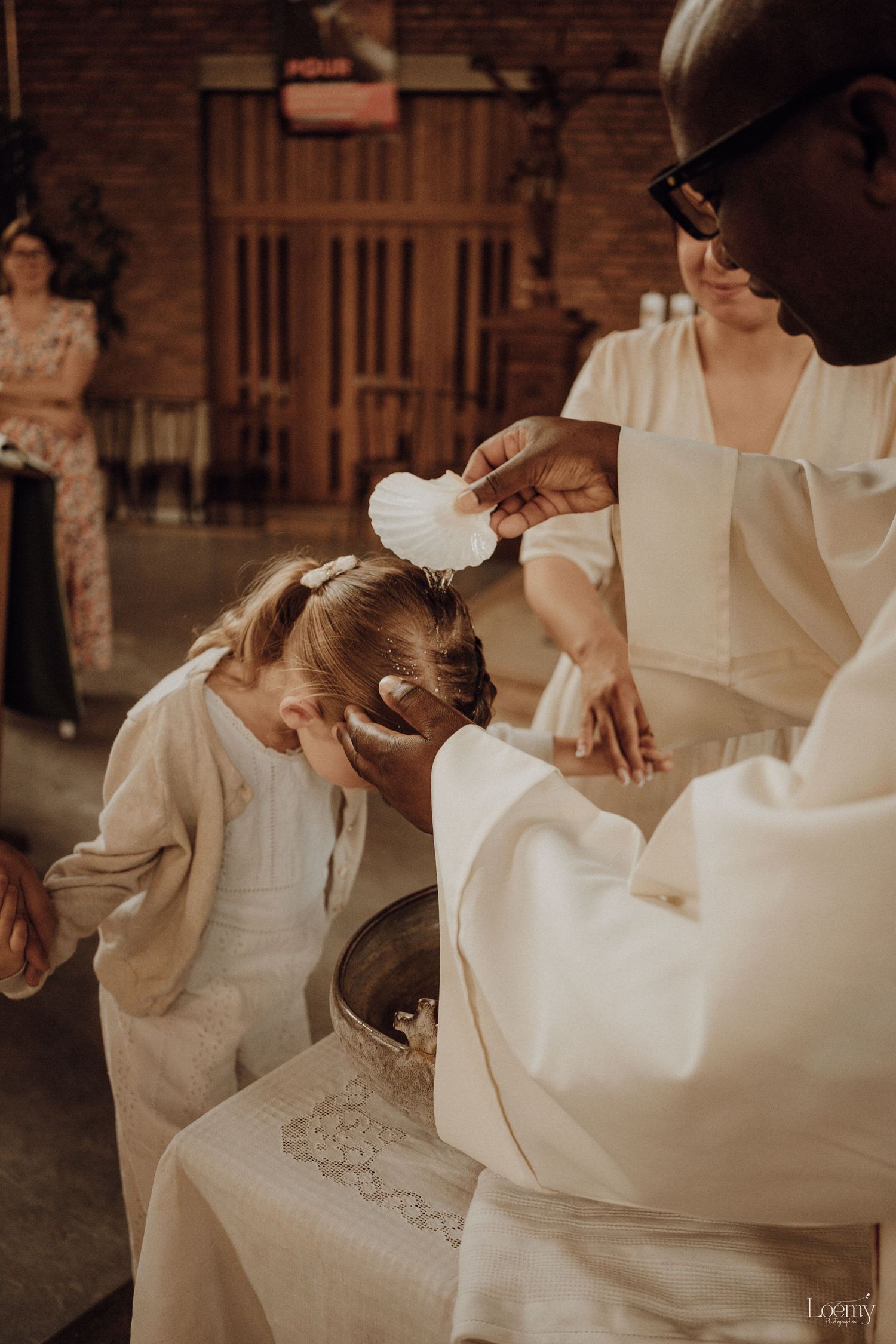 A priest pours water from a shell over a young girl's head during a baptism ceremony in a church.