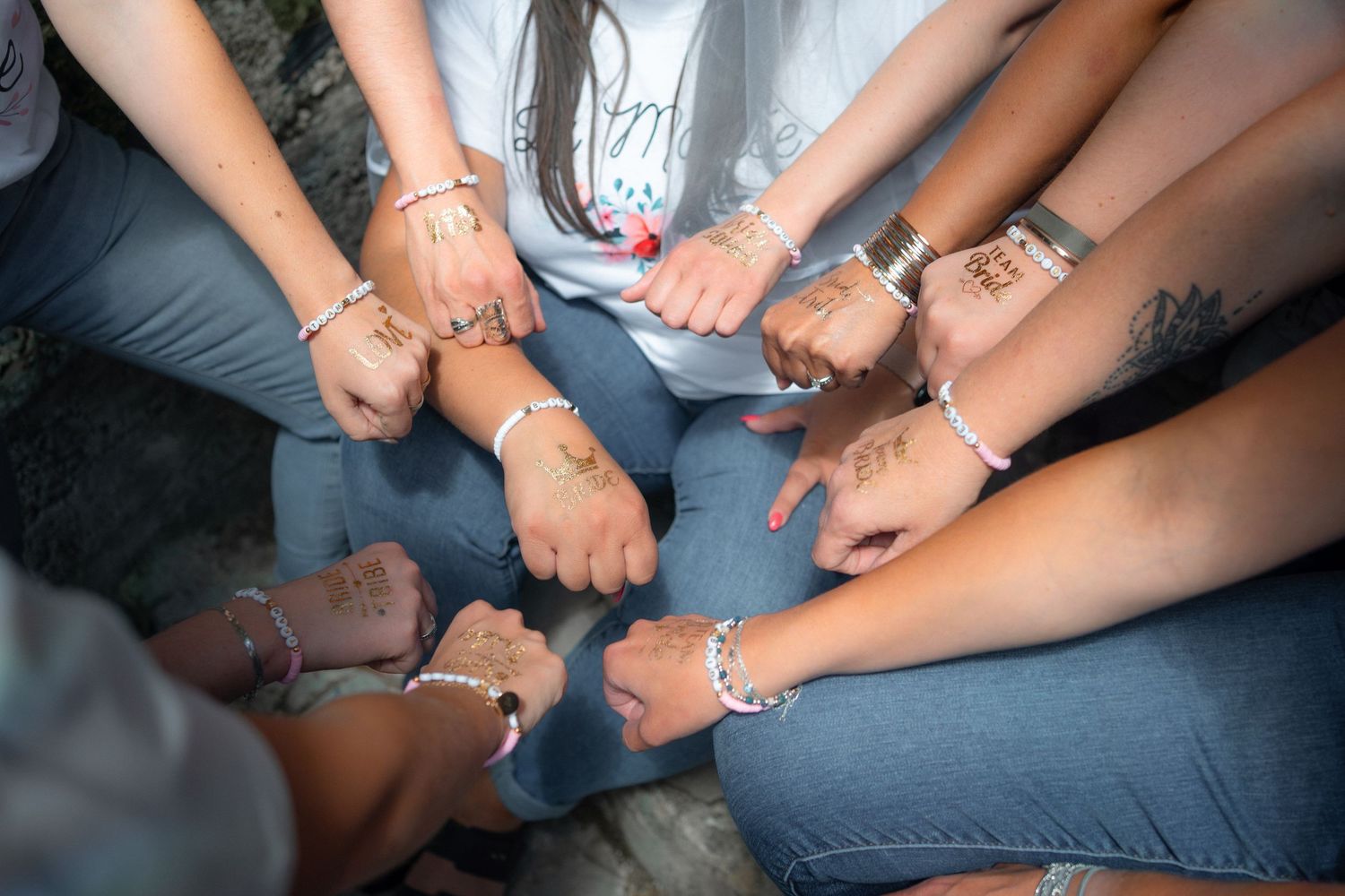 Group of women showing wrists with matching bracelets and henna tattoos in a circle huddle.