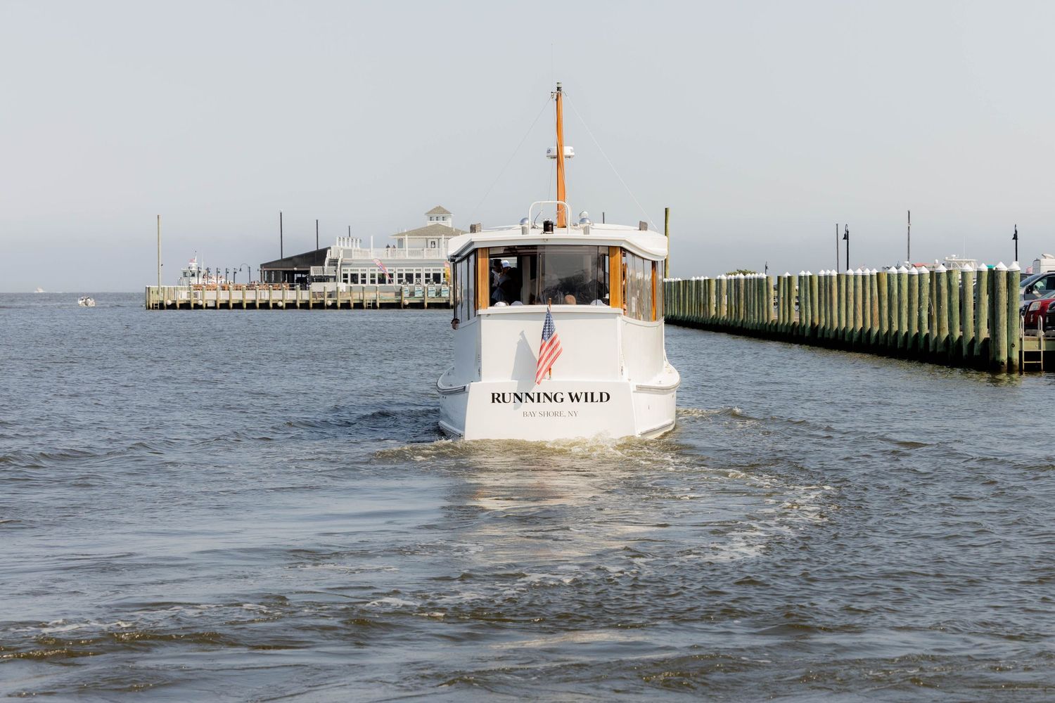 The stern view of boat 'Running Wild' sailing on open water with a pier in the background.