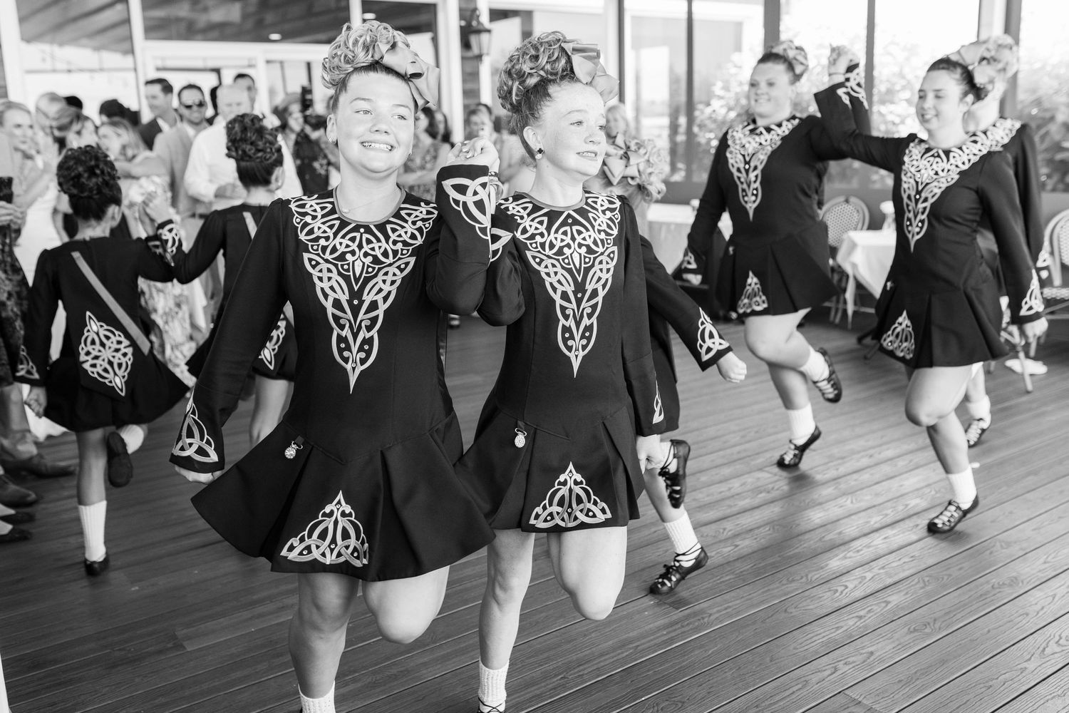 Dancers in vintage attire perform traditional Irish dance steps in a synchronized line on a wooden floor.