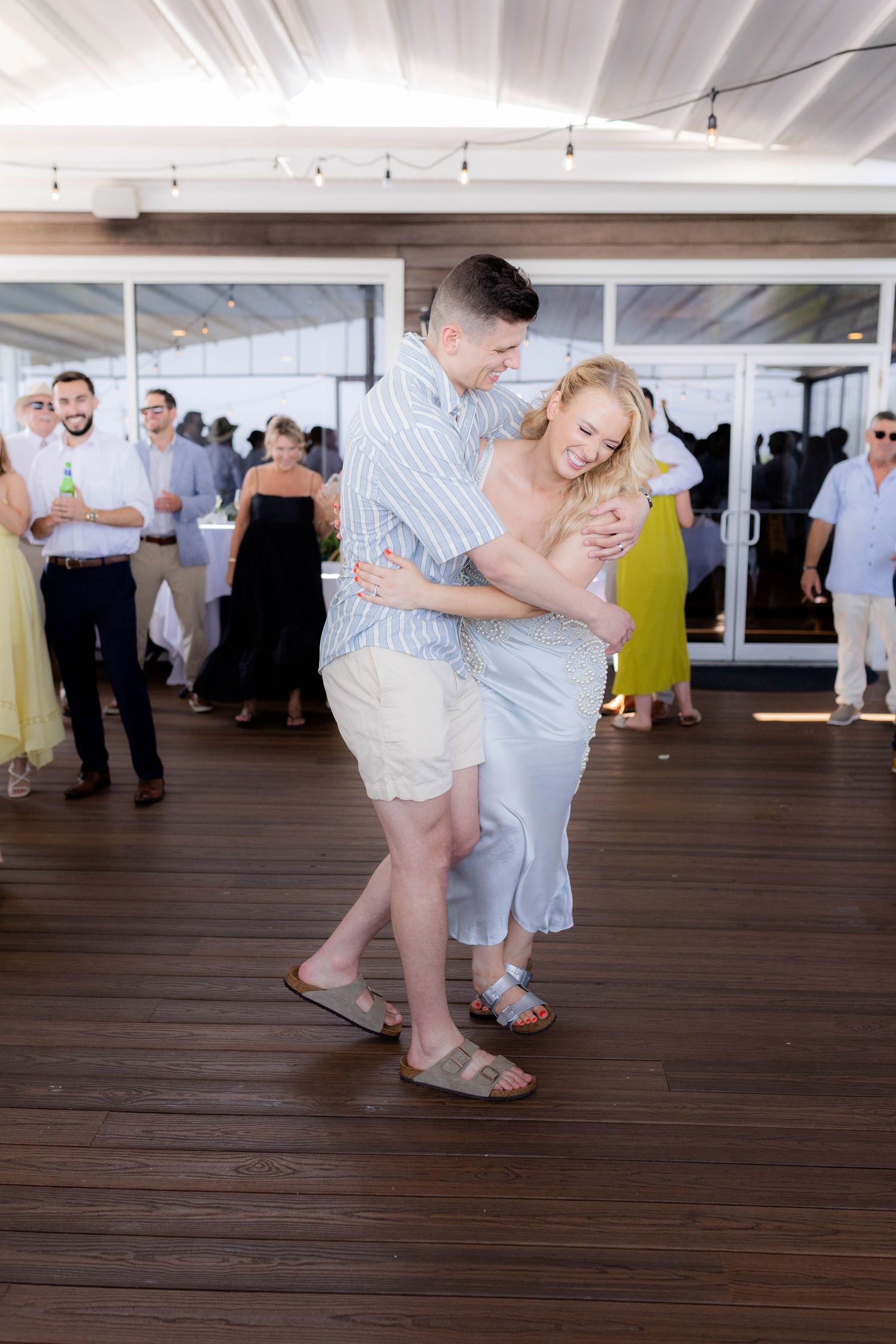 A couple shares a playful dance moment on a dark hardwood floor at an indoor event venue.