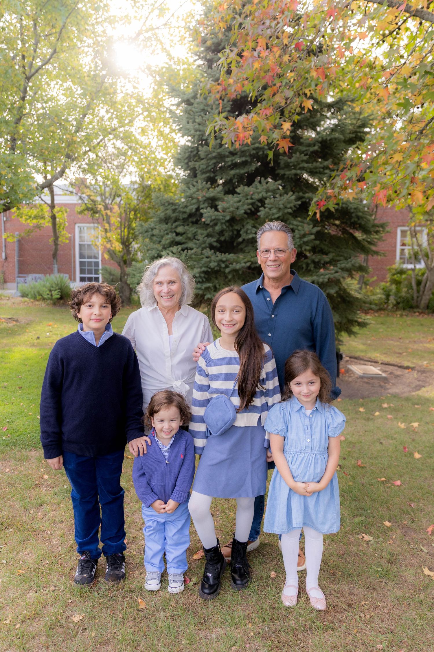 Family portrait session outdoors with autumn trees and brick building in background.