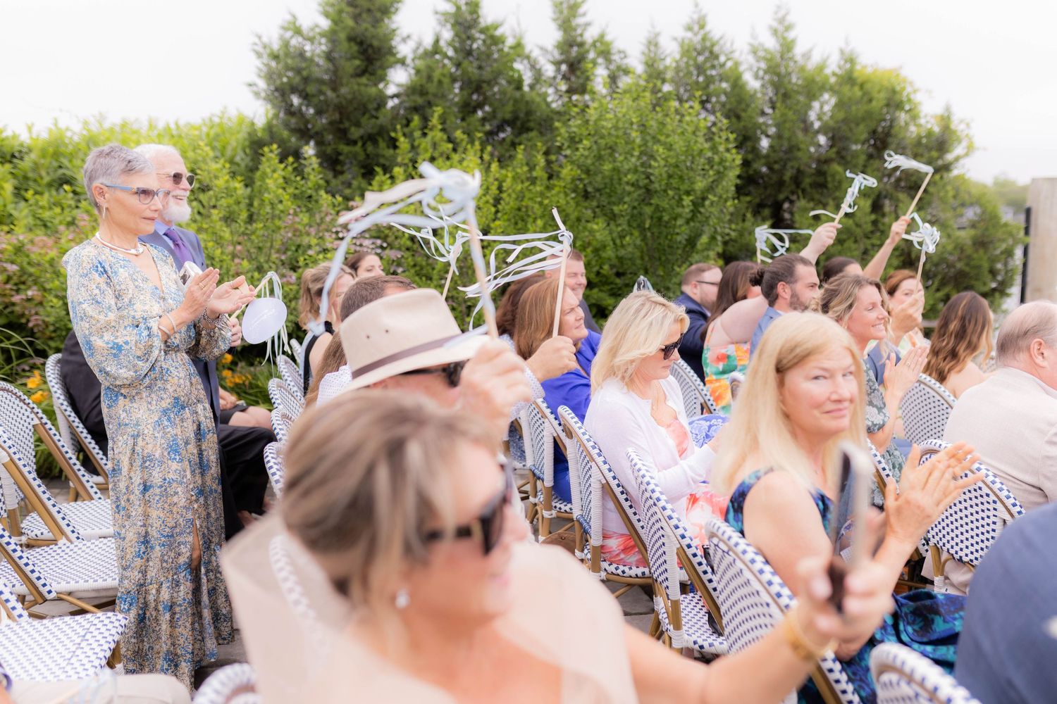 A group of guests raise their champagne glasses in a celebratory toast at an outdoor garden party.