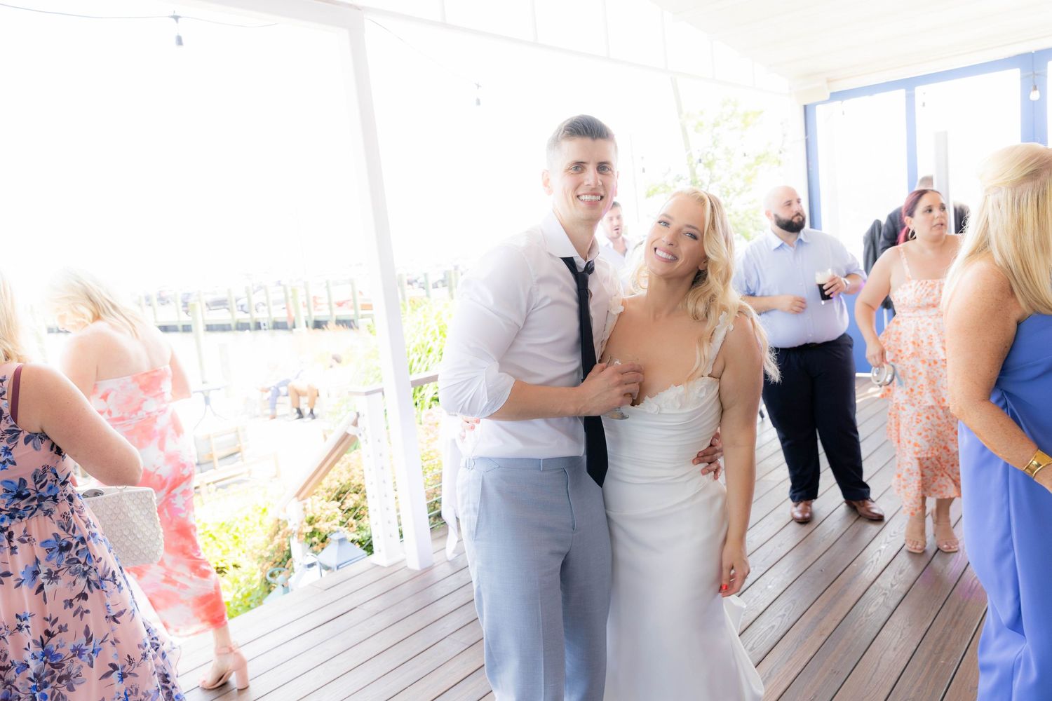 Wedding celebration on an outdoor deck with guests mingling and dancing in formal attire.