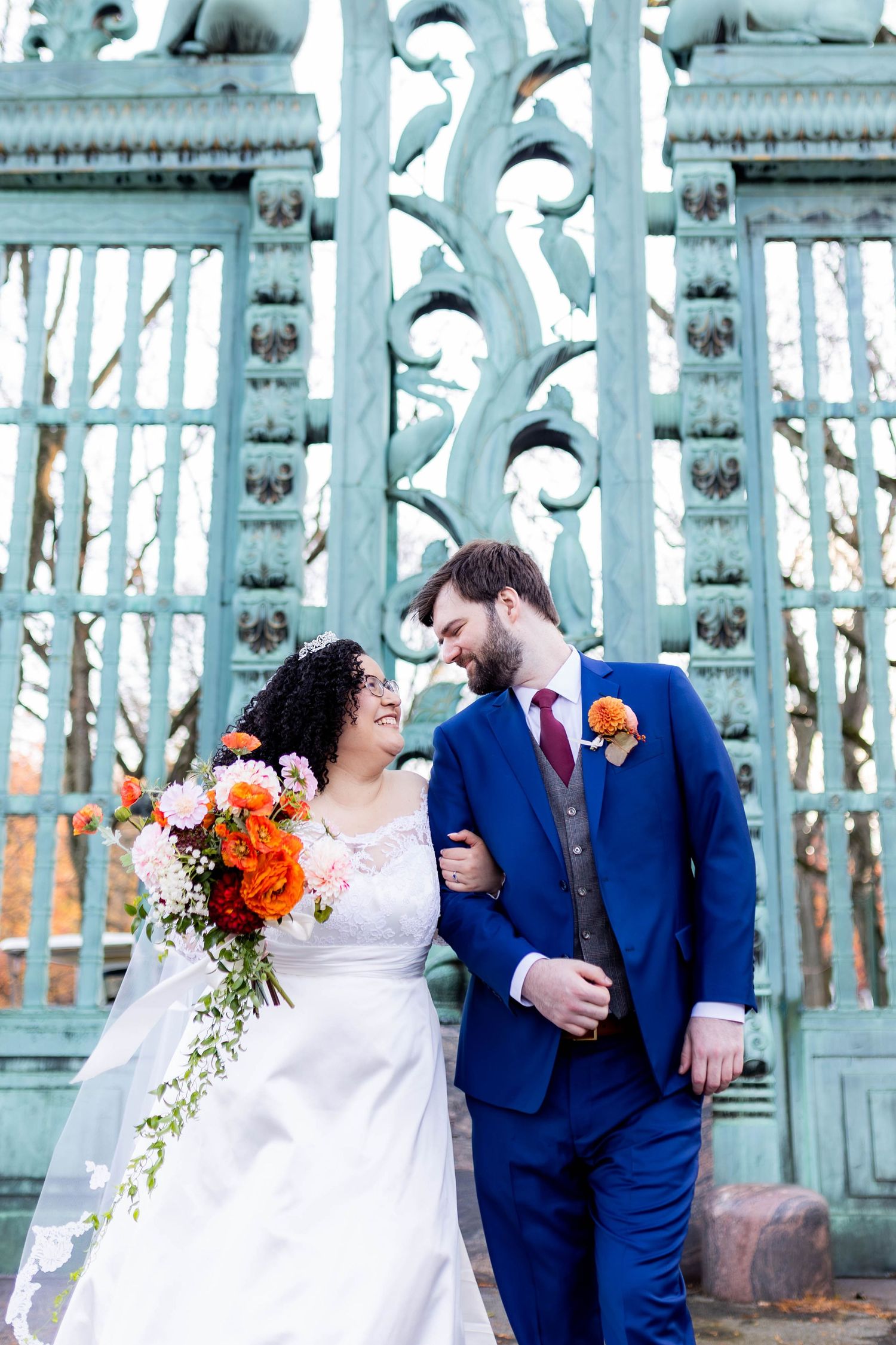 Wedding couple posing on blue industrial bridge with orange floral bouquet.