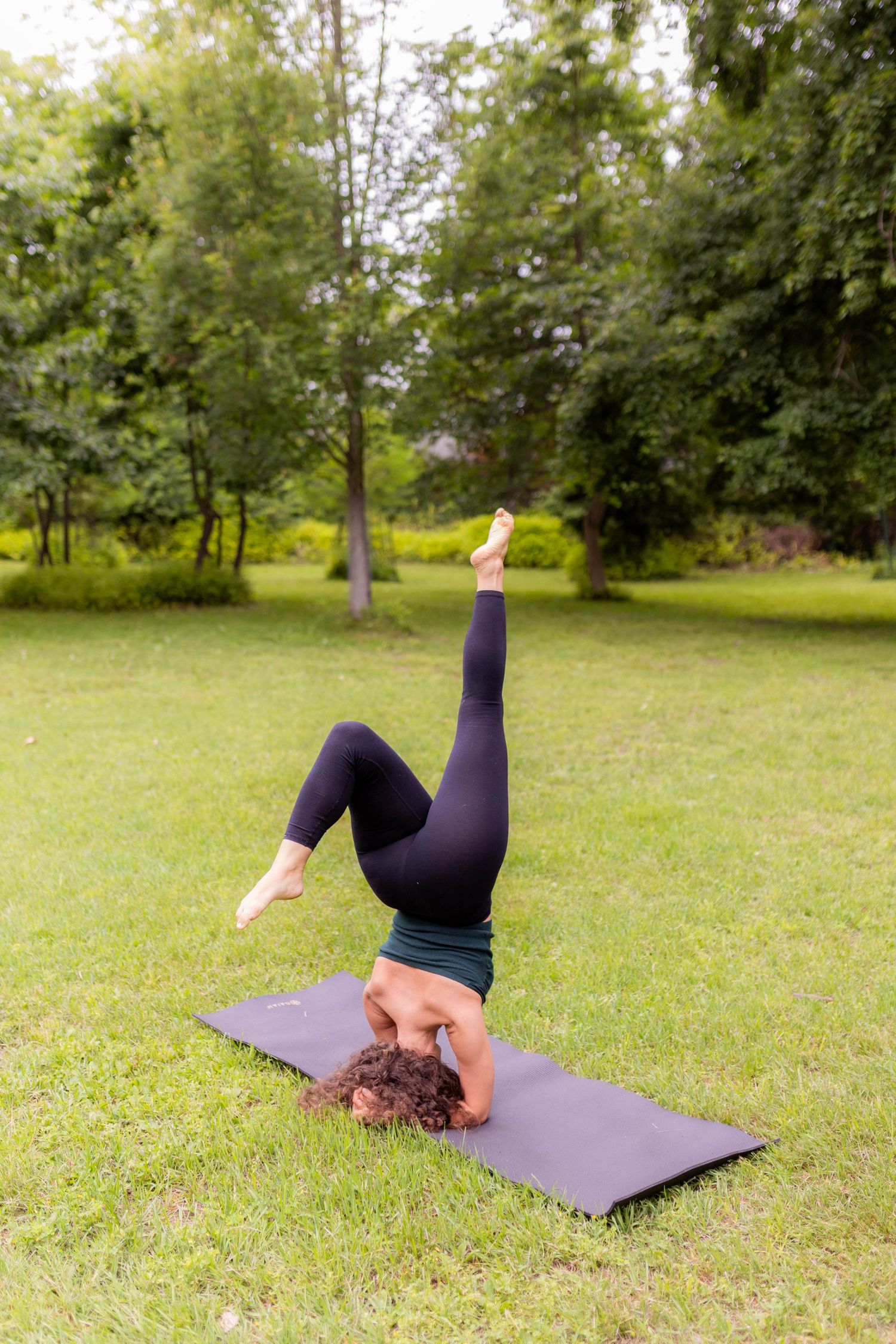 Yoga enthusiast performs headstand on purple exercise mat in park setting.
