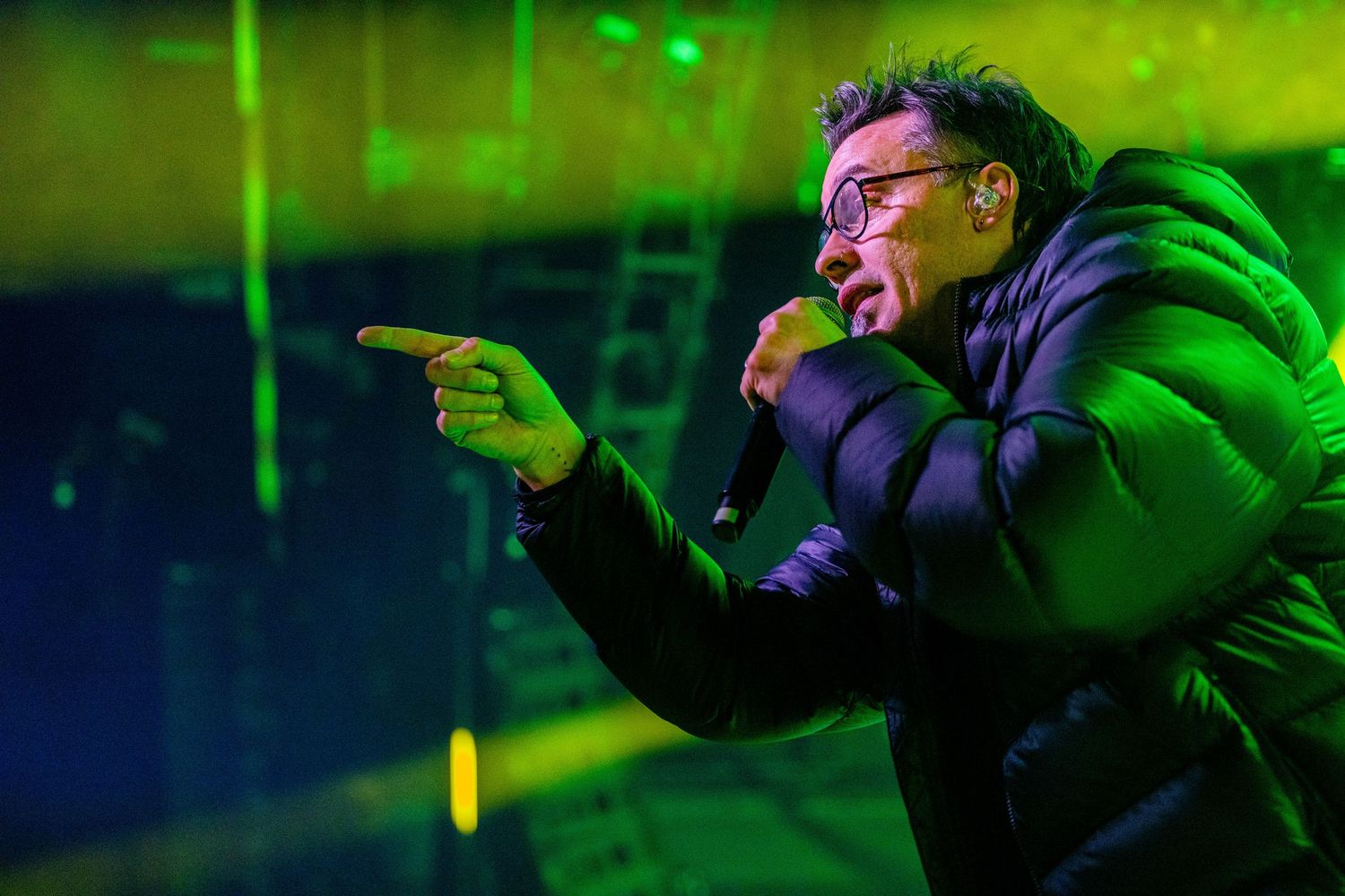 Concert stage bathed in vibrant green lighting with performer gesturing dramatically.