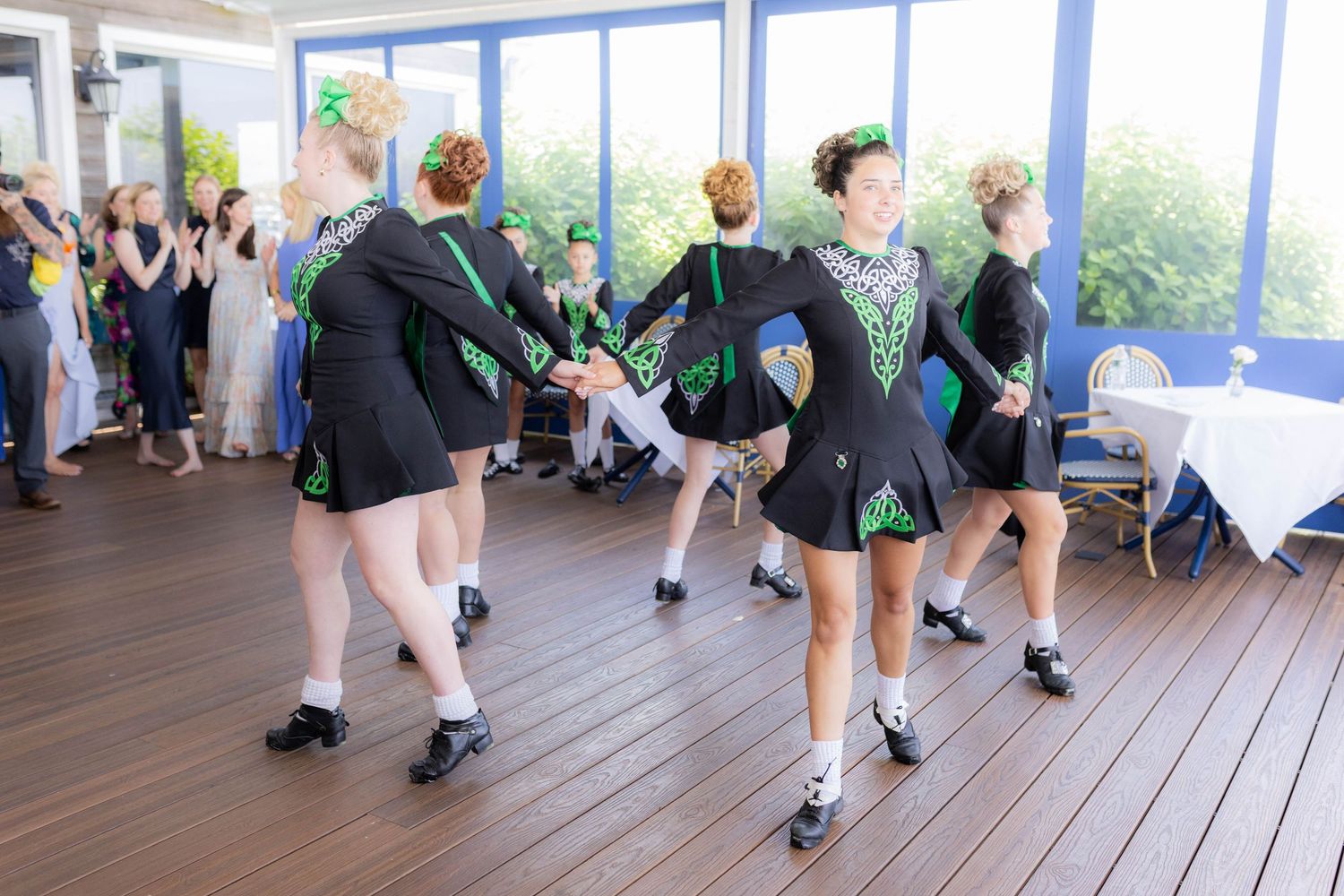 Irish step dancers showcase their footwork in matching costumes during a performance on an outdoor deck.
